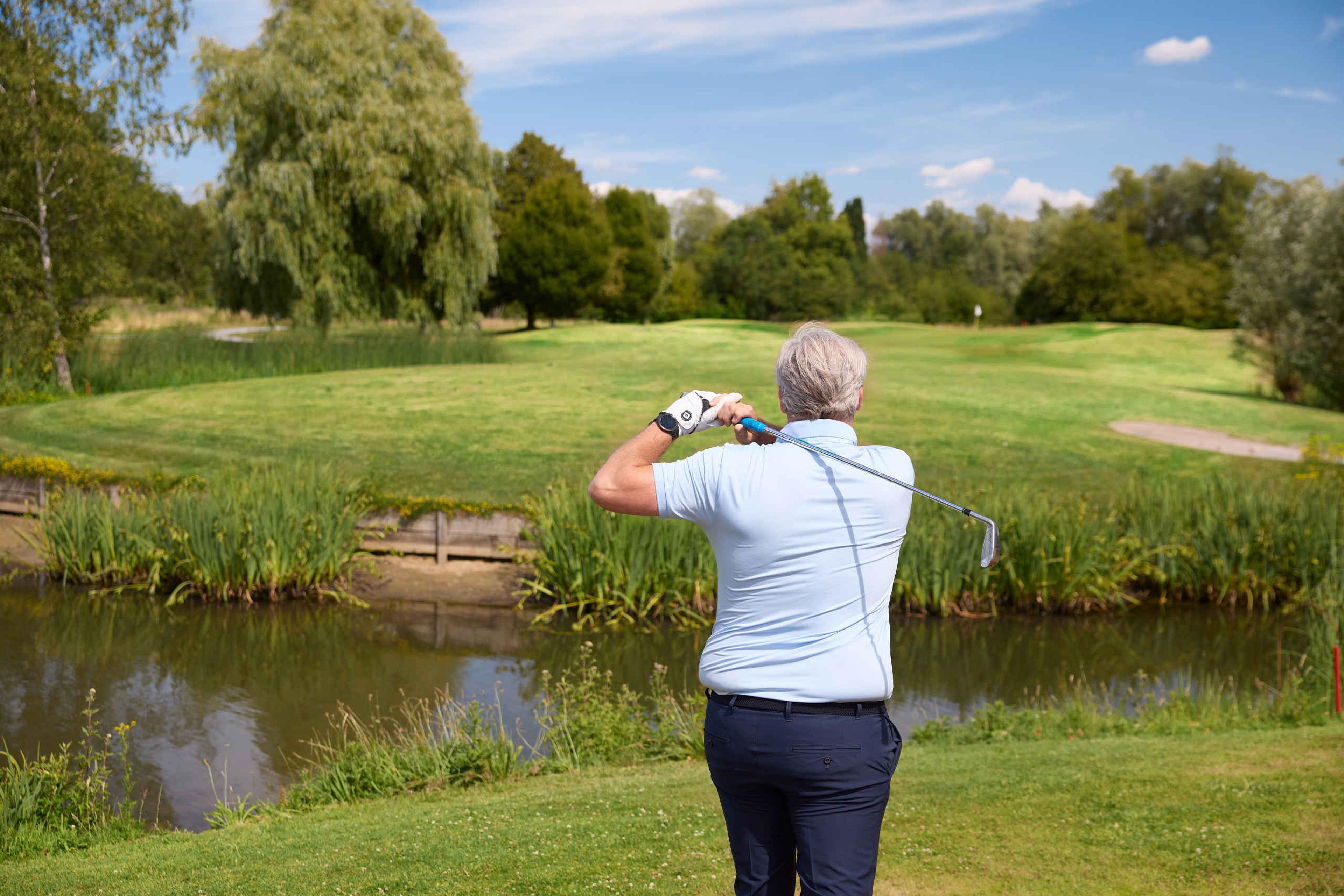 Een close-up van een man die zijn bal over het water slaat op de libellebaan van Golf De Gulbergen