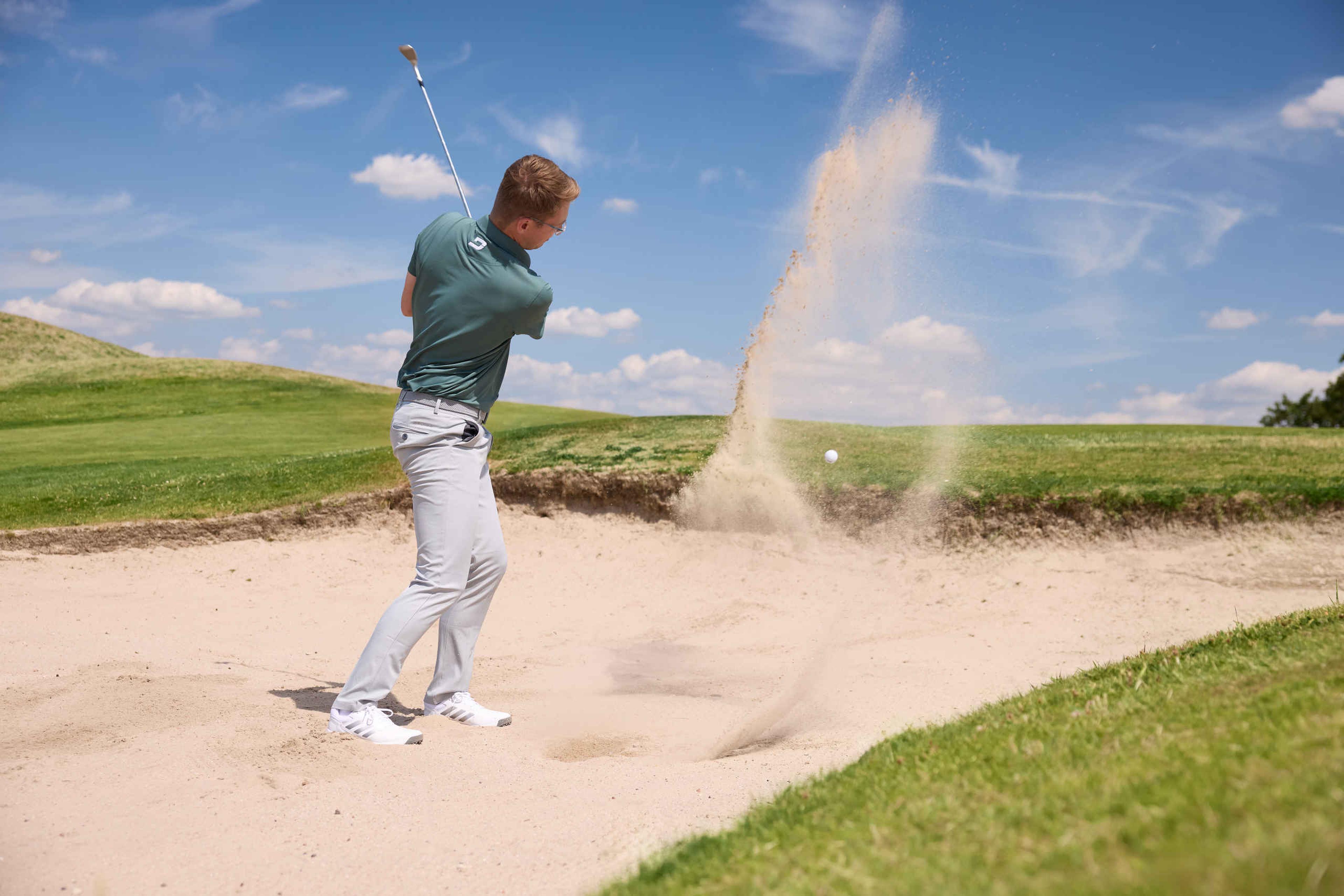 Een man slaat een bal uit de bunker op de Sprookjesbaan van Golf De Gulbergen