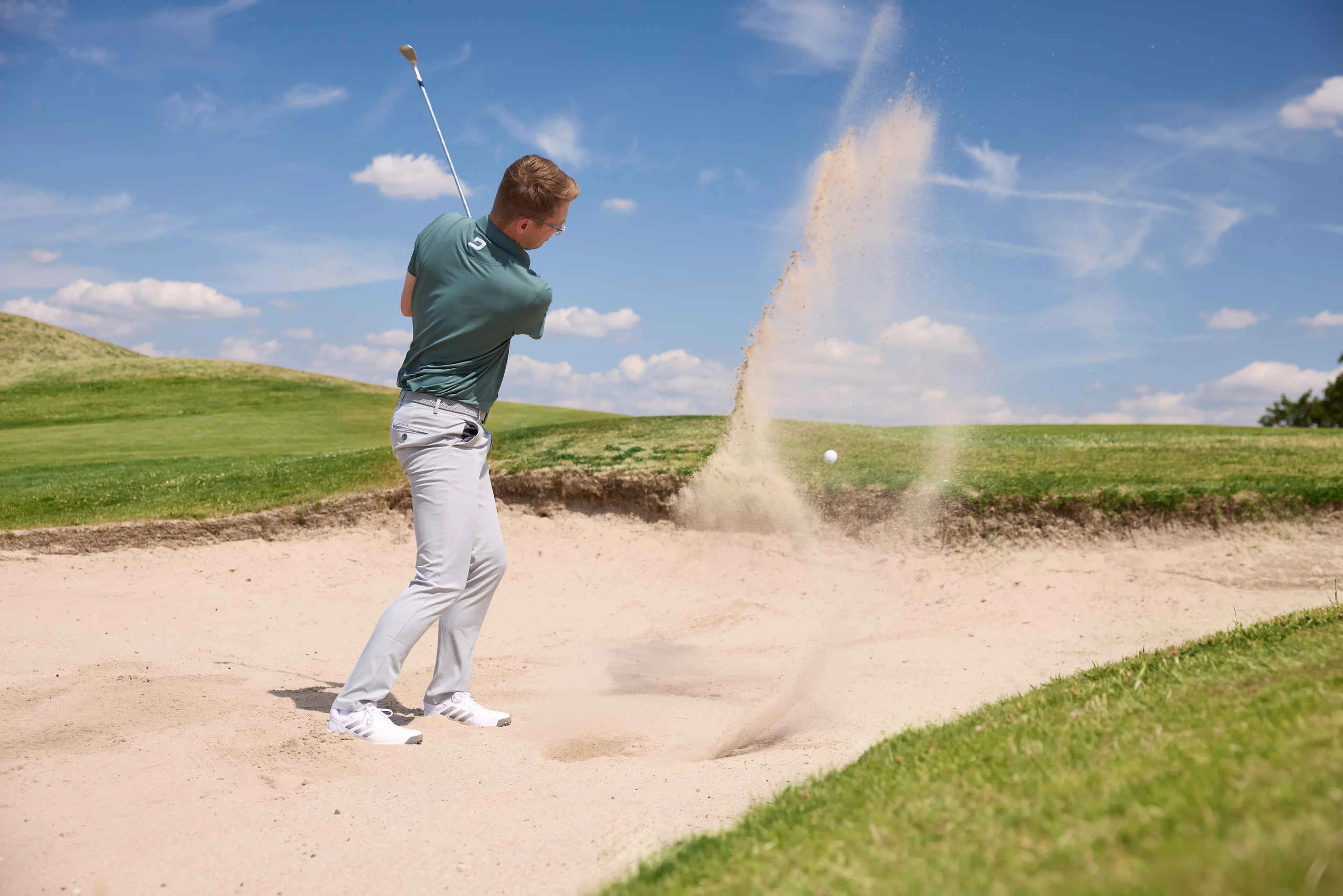 Een man slaat een bal uit de bunker op de Sprookjesbaan van Golf De Gulbergen