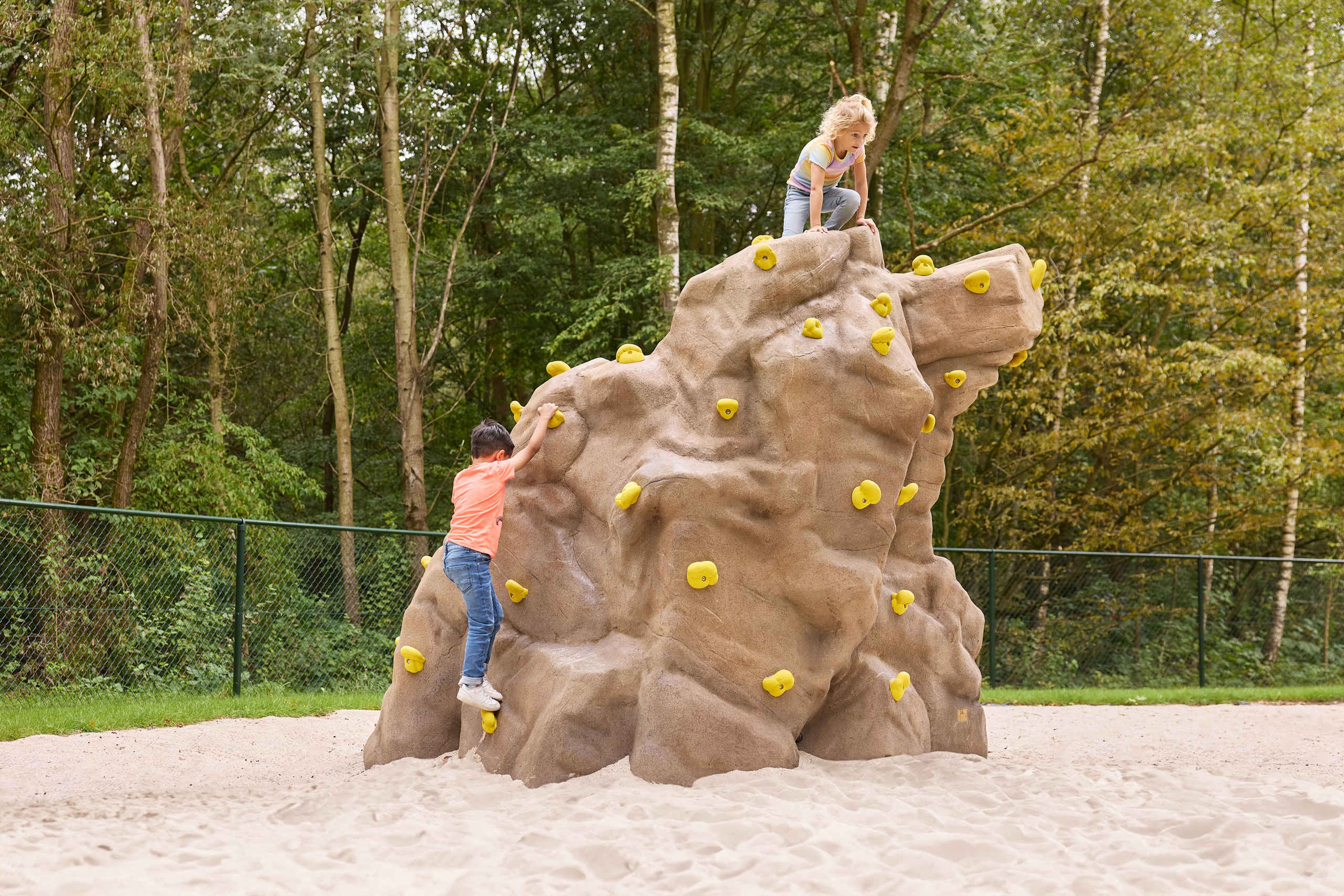 Een jongen en een meisje klimmen op een klimsteen in het boulderpark van Klimrijk Brabant.