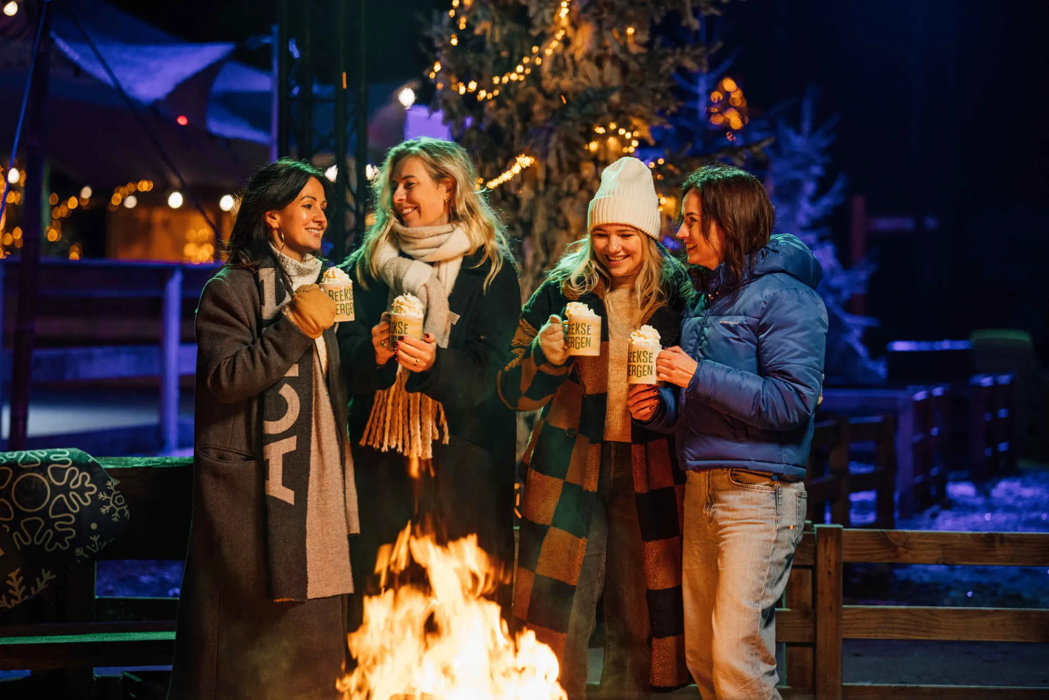 Een groep collega's staat rond het kampvuur met warme chocolademelk bij Light Safari Beekse Bergen.