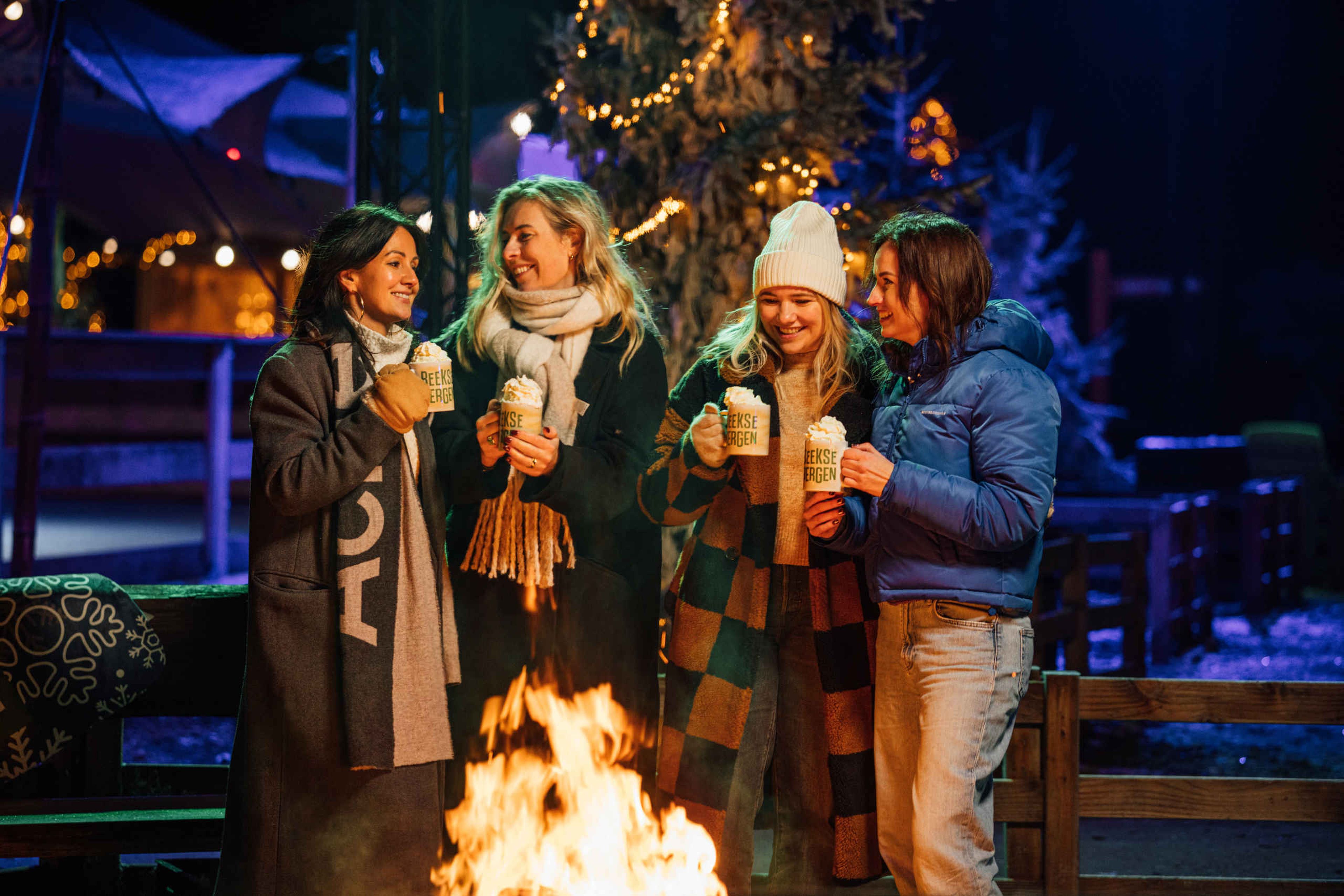 Een groep collega's staat rond het kampvuur met warme chocolademelk bij Light Safari Beekse Bergen.