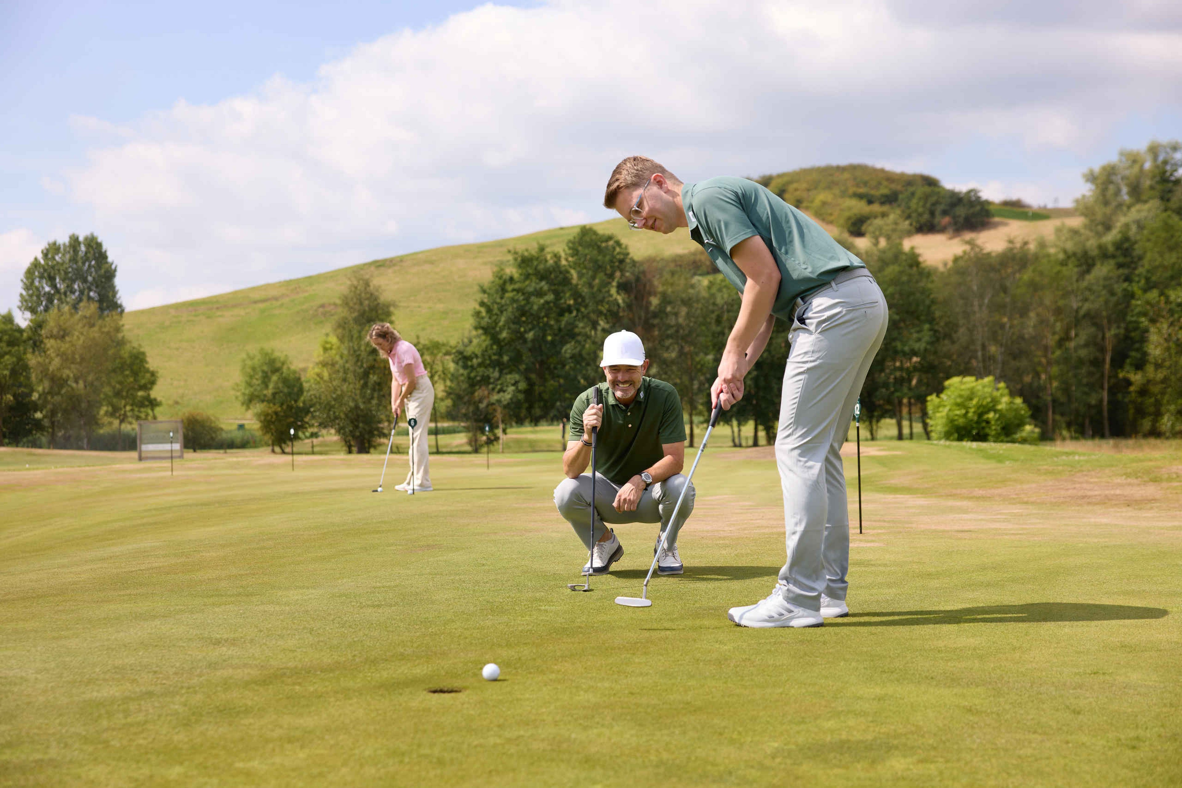 Een man putt zijn bal terwijl de golfpro van de golfacademy toekijkt op de puttinggreen van Golf De Gulbergen