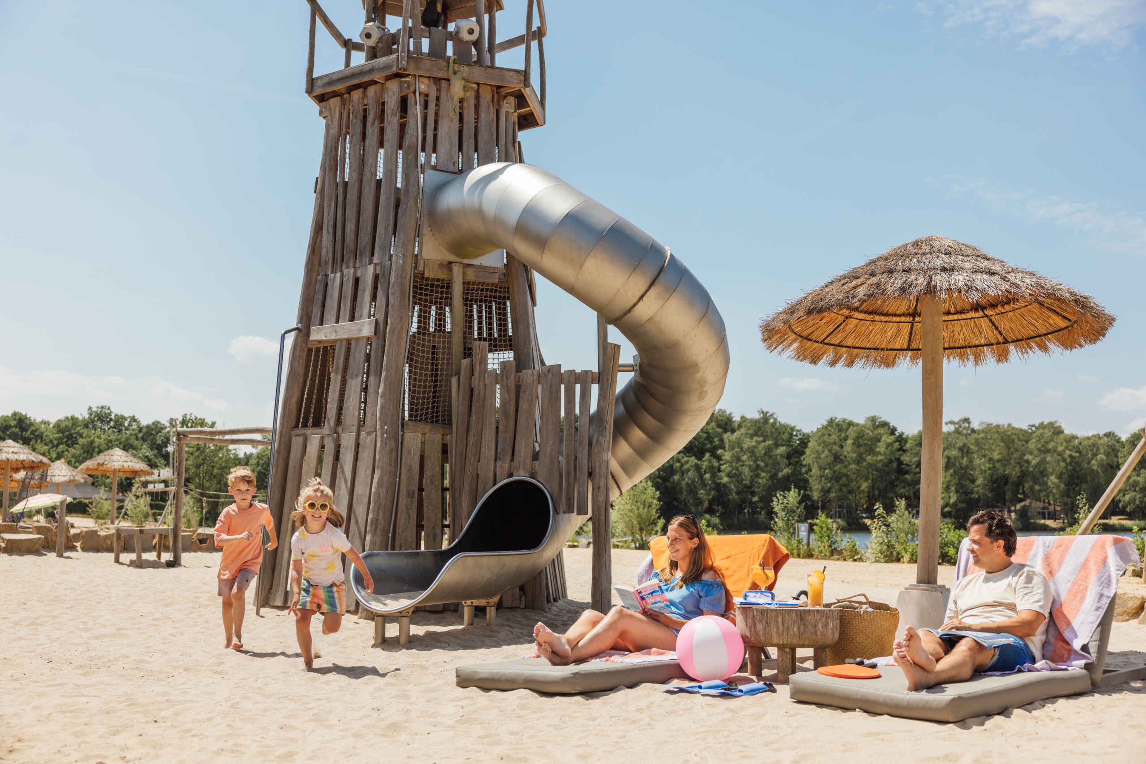 Twee kinderen spelen op het strand terwijl hun ouders op een bedje liggen te zonnen bij Lake Resort Beekse Bergen.