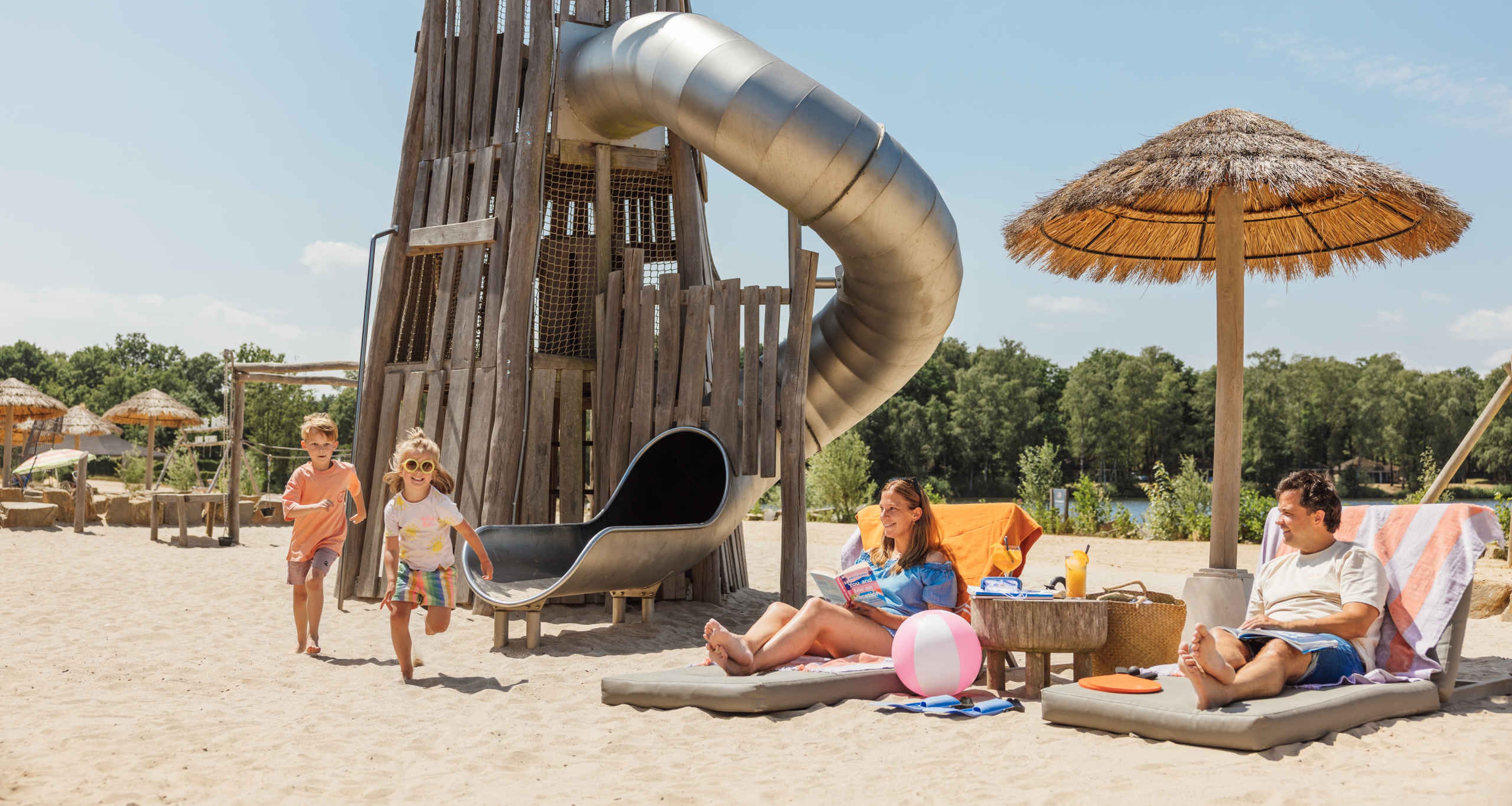 Twee kinderen spelen op het strand terwijl hun ouders op een bedje liggen te zonnen bij Lake Resort Beekse Bergen.