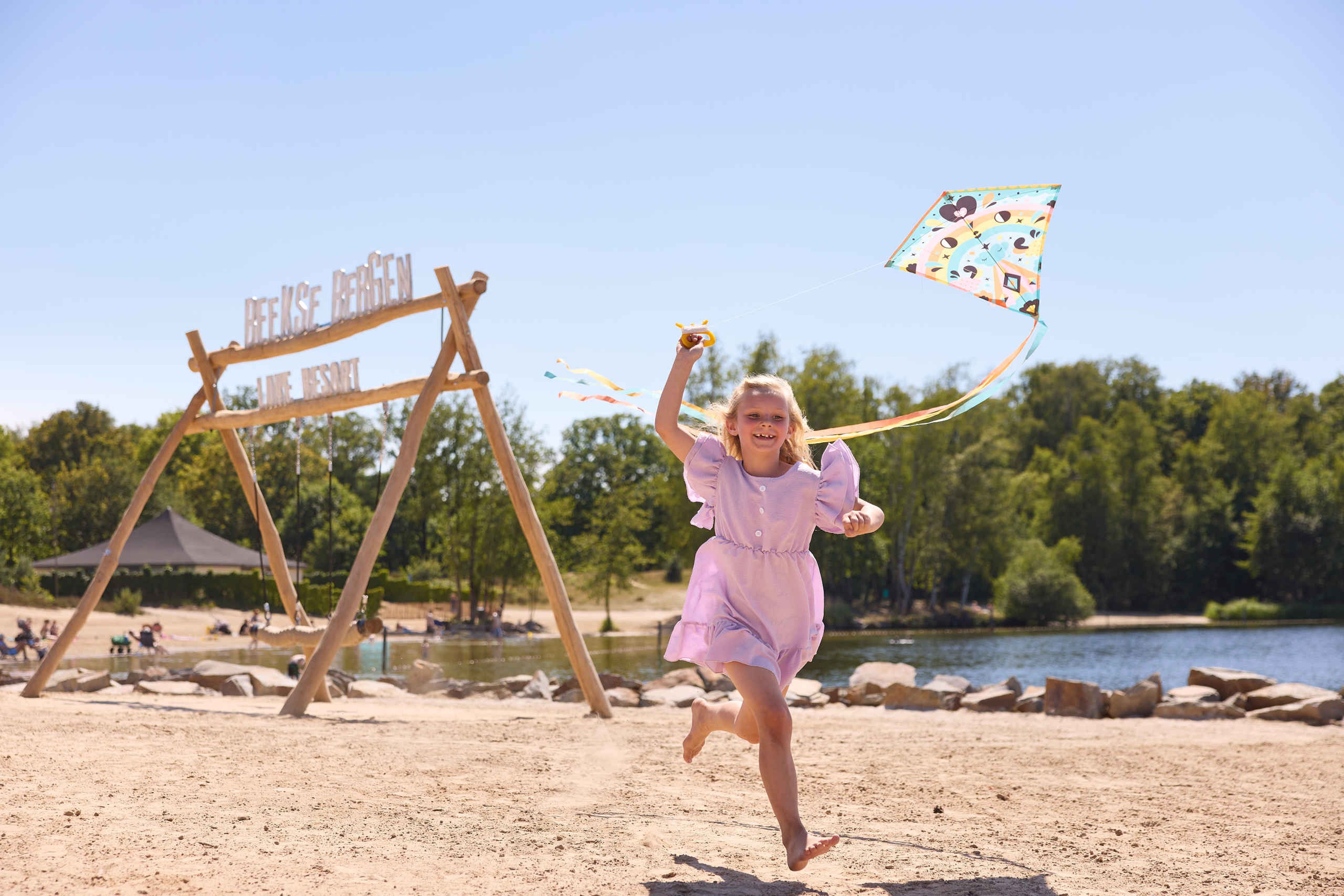 Een meisje rent met haar vlieger over het strand bij het Victoriameer van Lake Resort Beekse Bergen