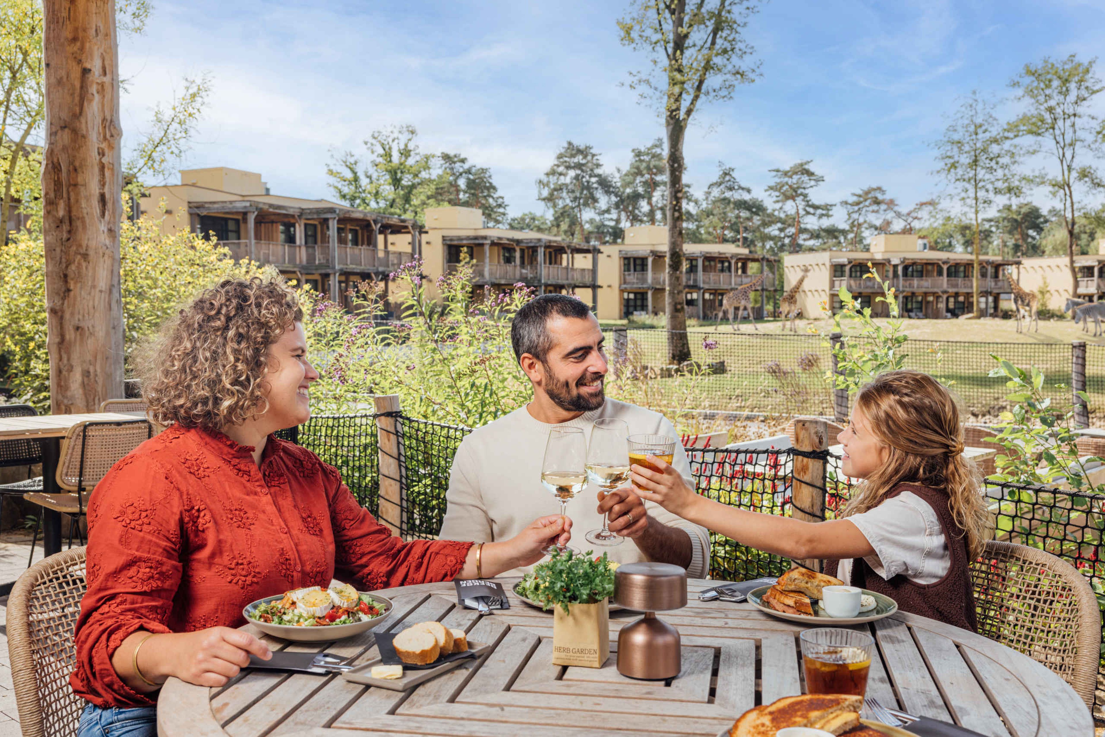 In de lente uitzicht op de giraffen ouders meet meisje lunchen buiten op het terras van Safari Hotel Beekse Bergen
