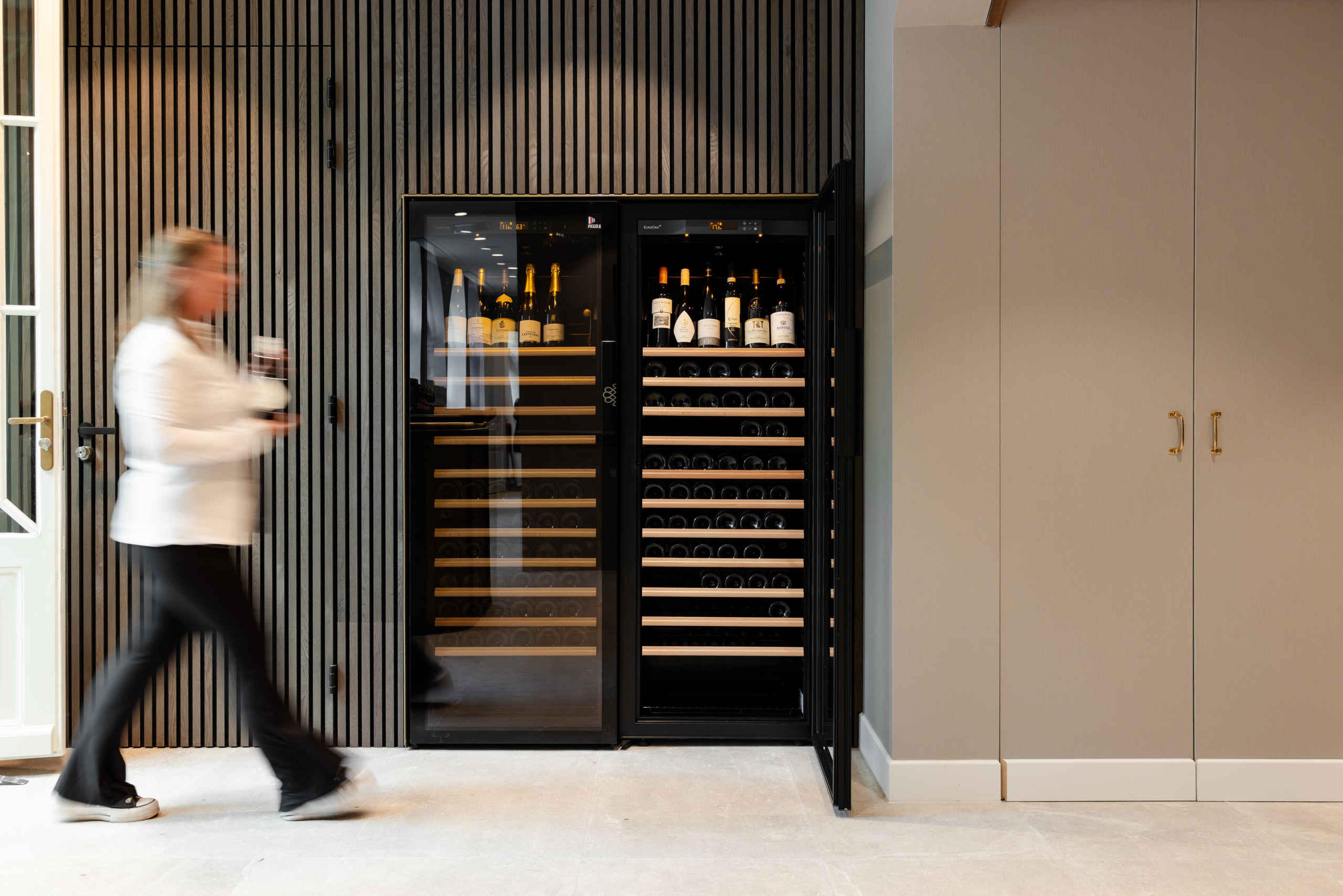 Een serveerster loopt langs de wijnkast bij Orangerie Steenenburg.