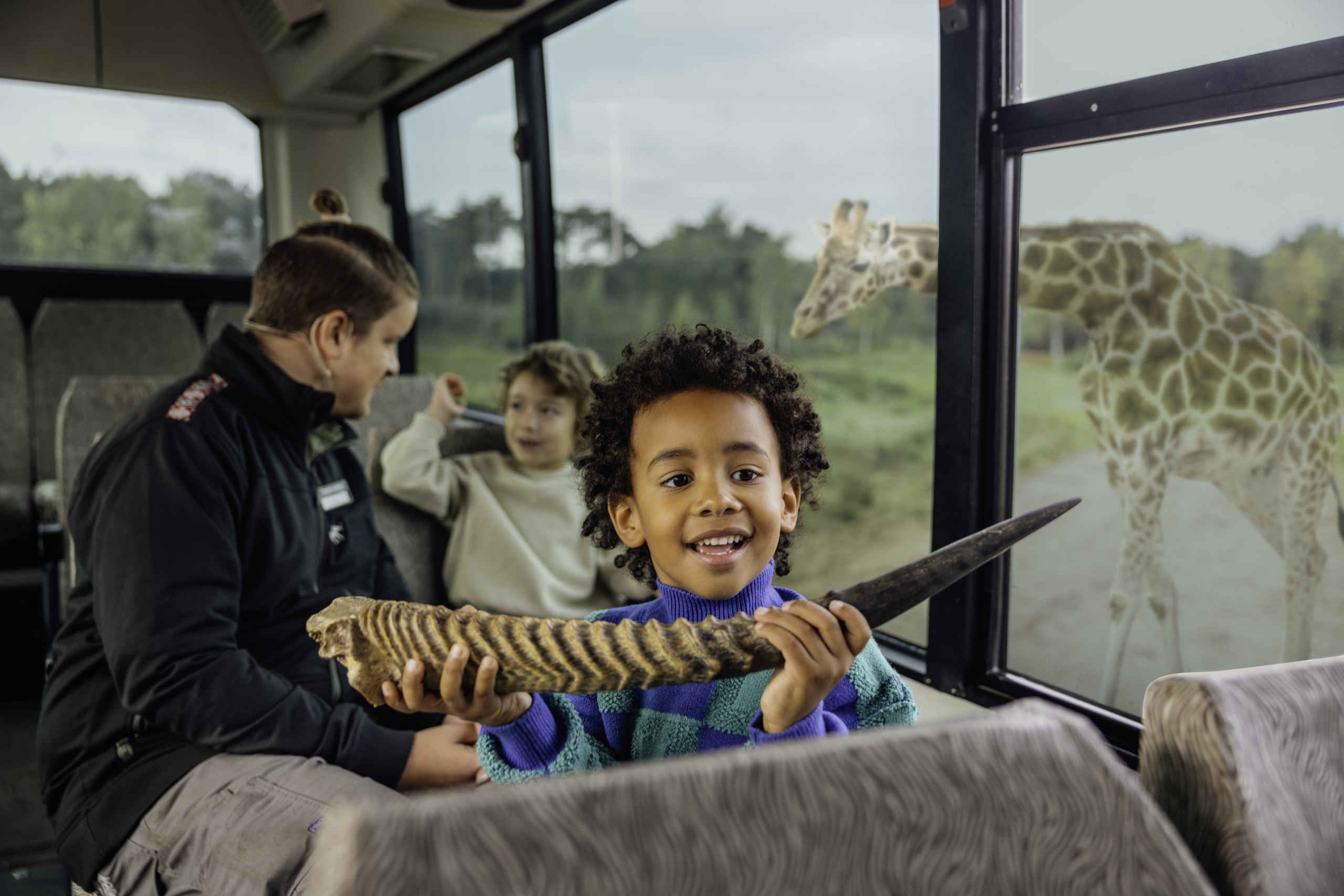 Bussafari rangers met jongens en een giraffe in Safaripark Beekse Bergen