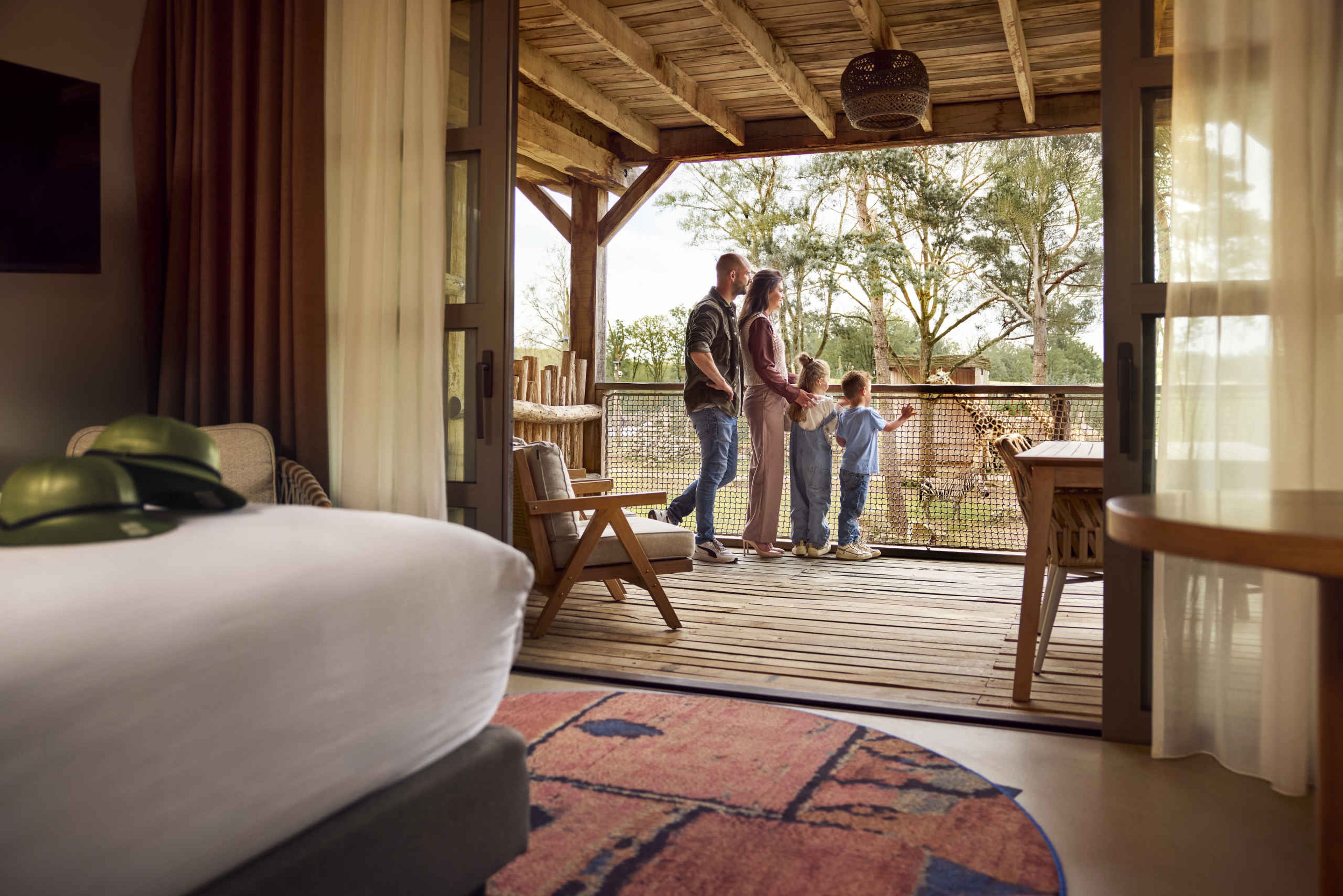 Een gezin kijkt naar een giraf op het terras van een Savanne Room bij het Safari Hotel Beekse Bergen.