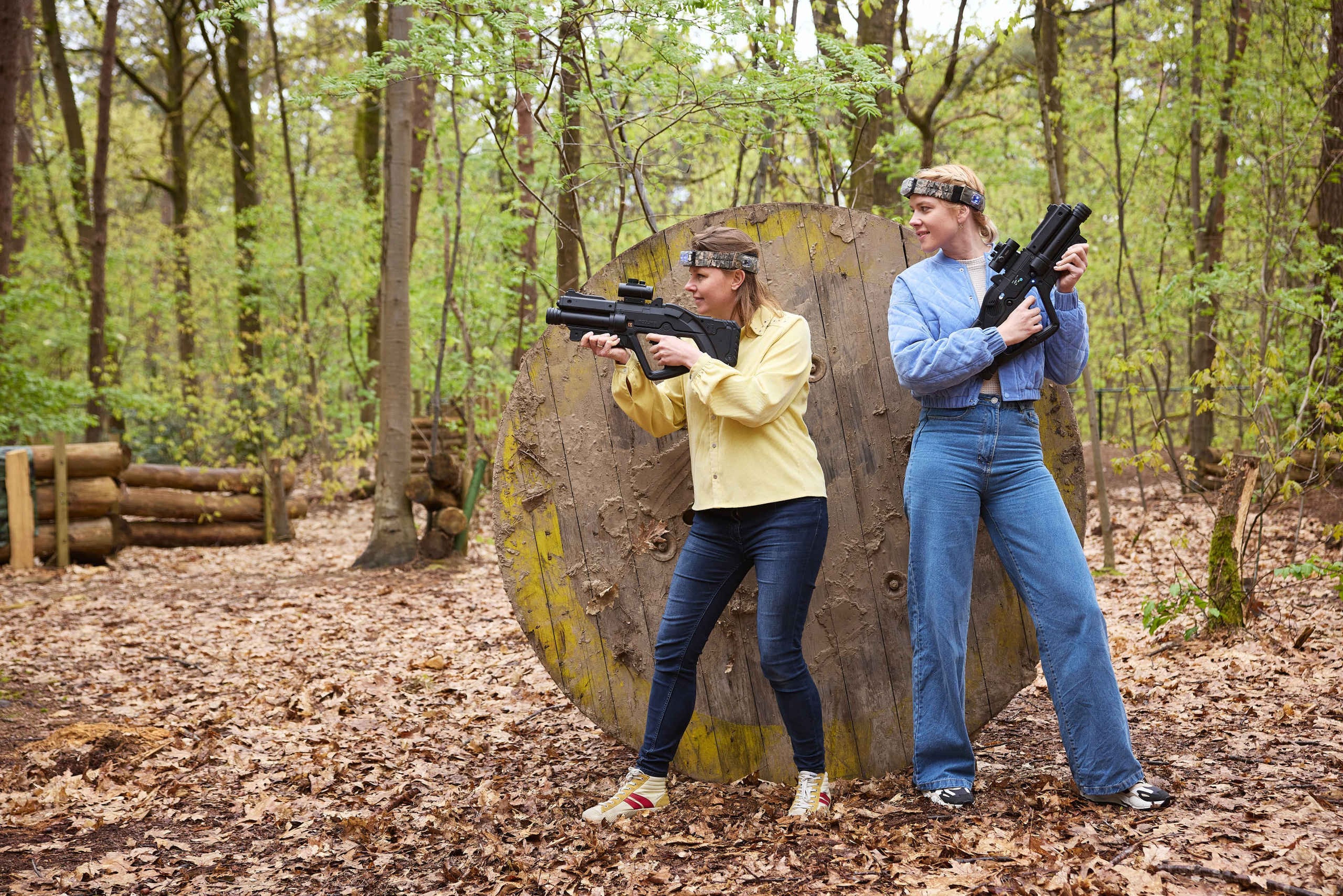 Twee vrouwen spelen outdoor lasergamen en verstoppen zich achter een obstakel bij Klimrijk Brabant.