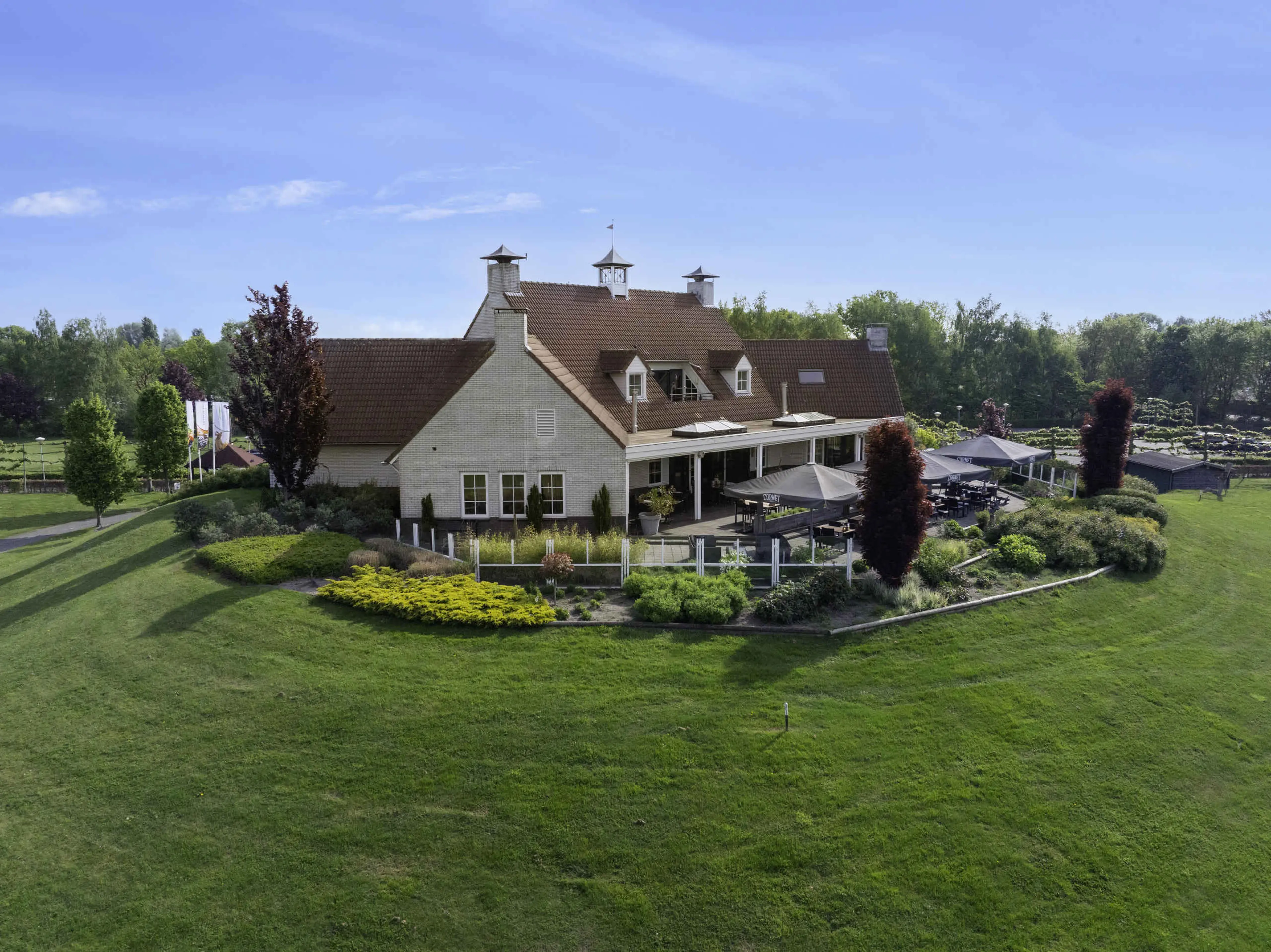 Het Clubhuis en terras met parasols in de zomer bij Golf De Gulbergen