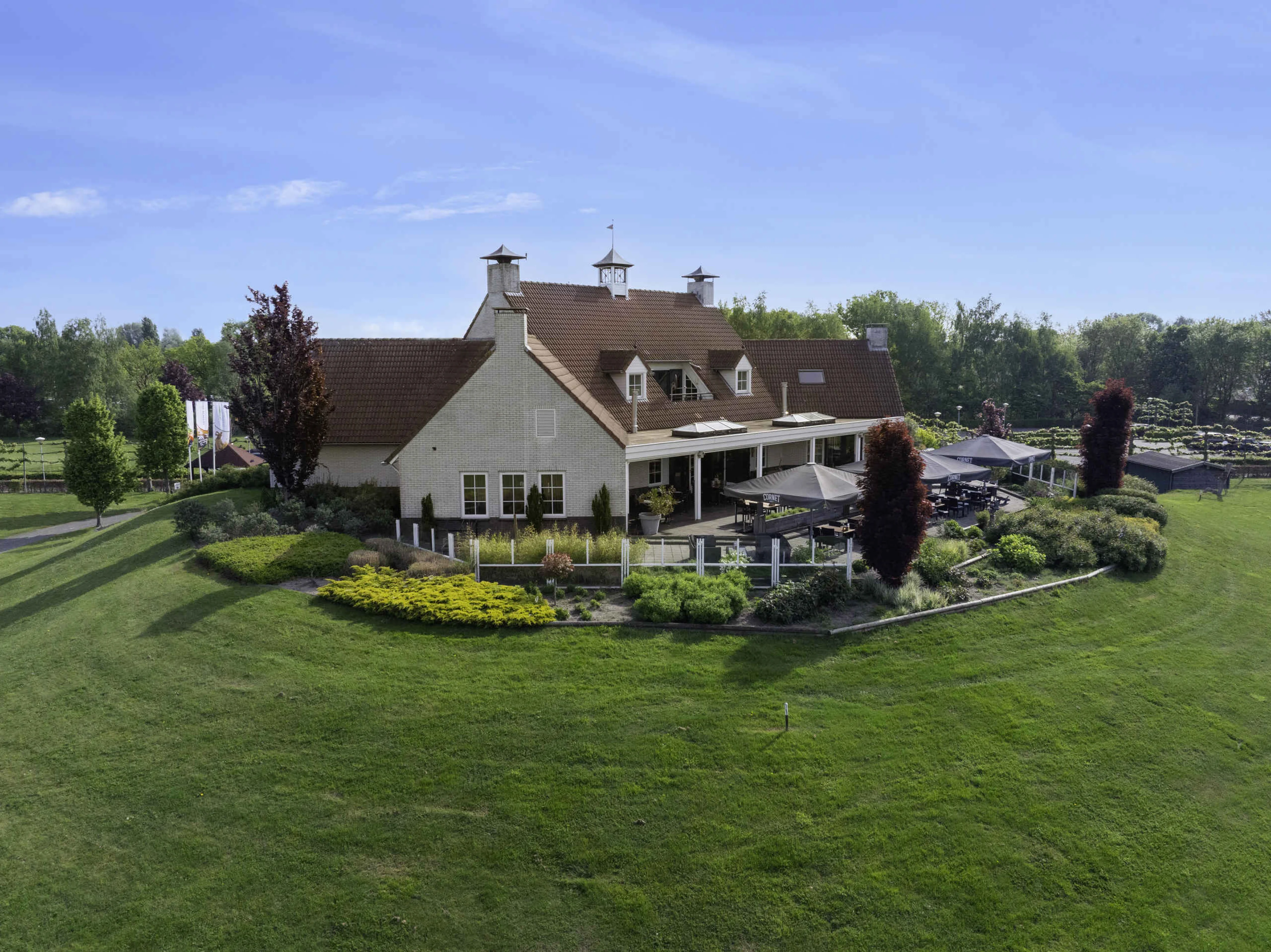 Het Clubhuis en terras met parasols in de zomer bij Golf De Gulbergen