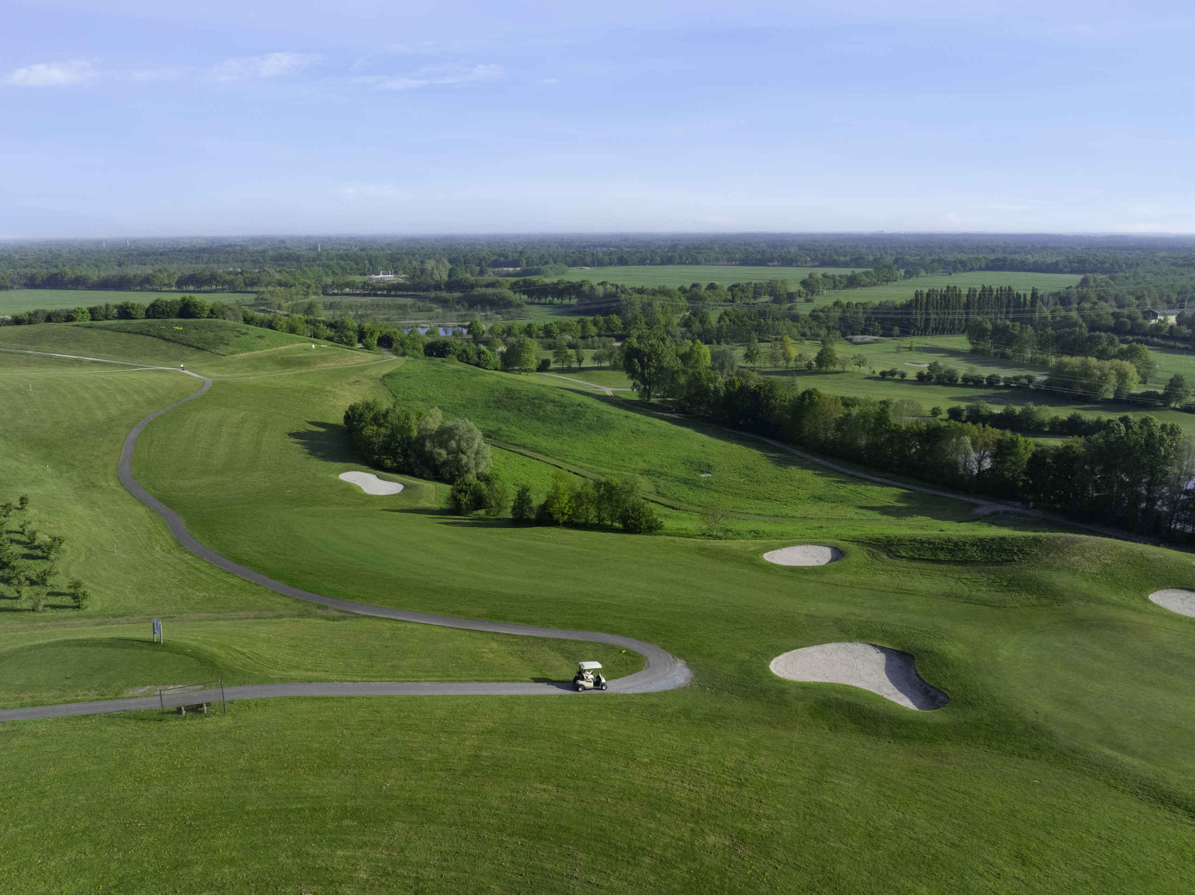 Een droneshot van de fairway en green van hole 2 met in de verte de libellebaan bij Golf De Gulbergen