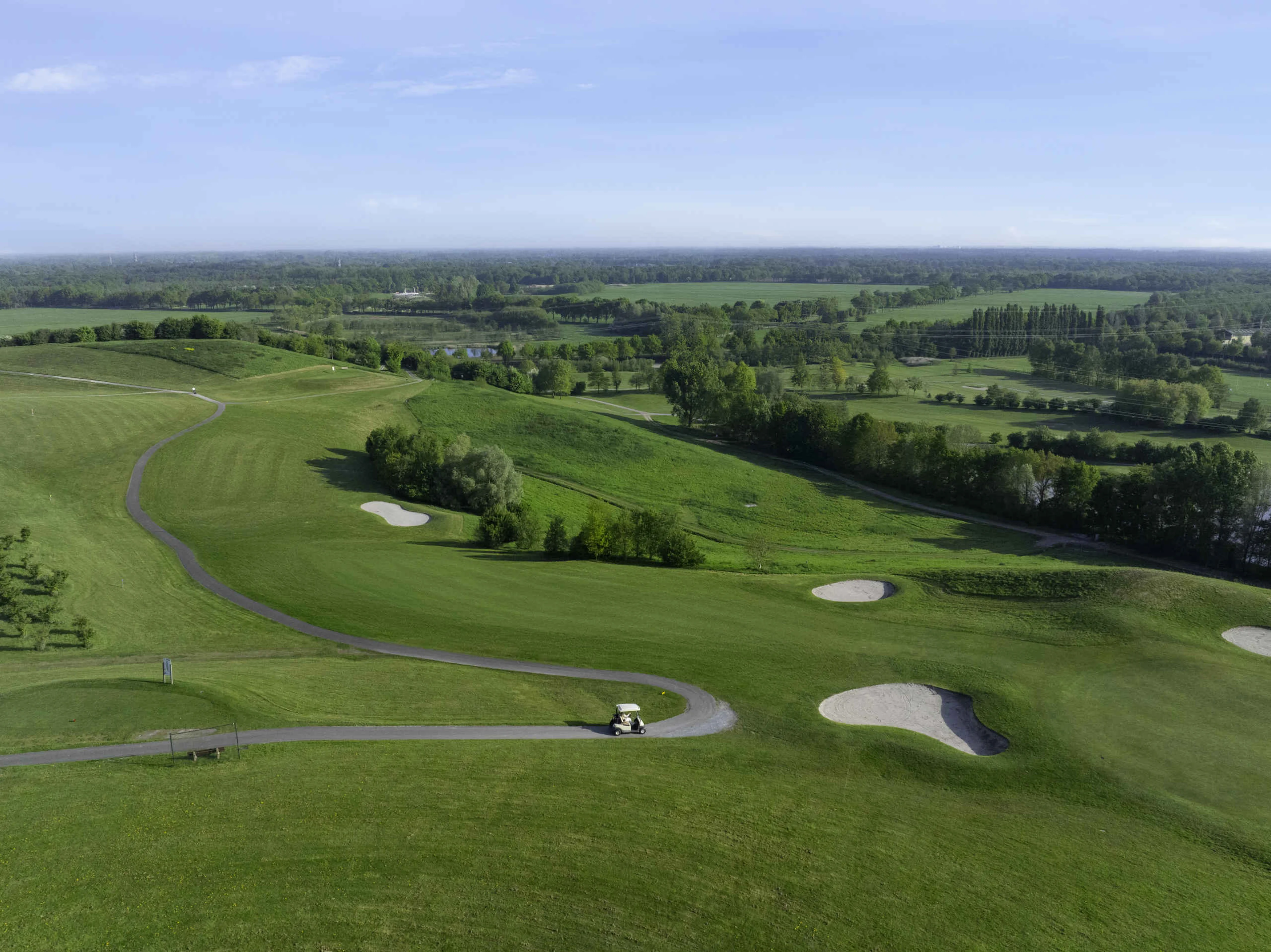 Een droneshot van de fairway en green van hole 2 met in de verte de libellebaan bij Golf De Gulbergen