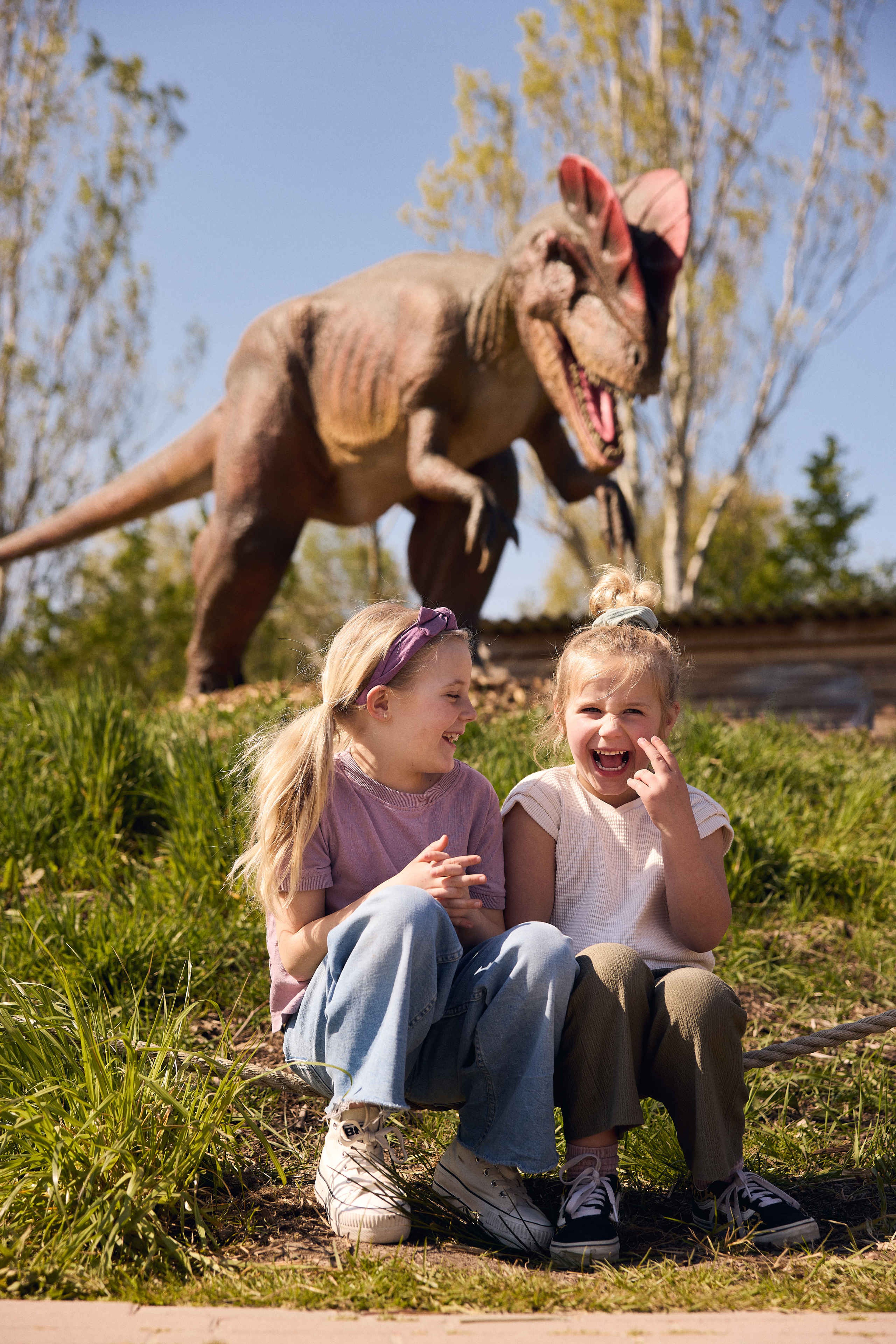 Twee meisjes zitten in de zon in het gras tijdens DINO vs DIER bij Eindhoven Zoo.