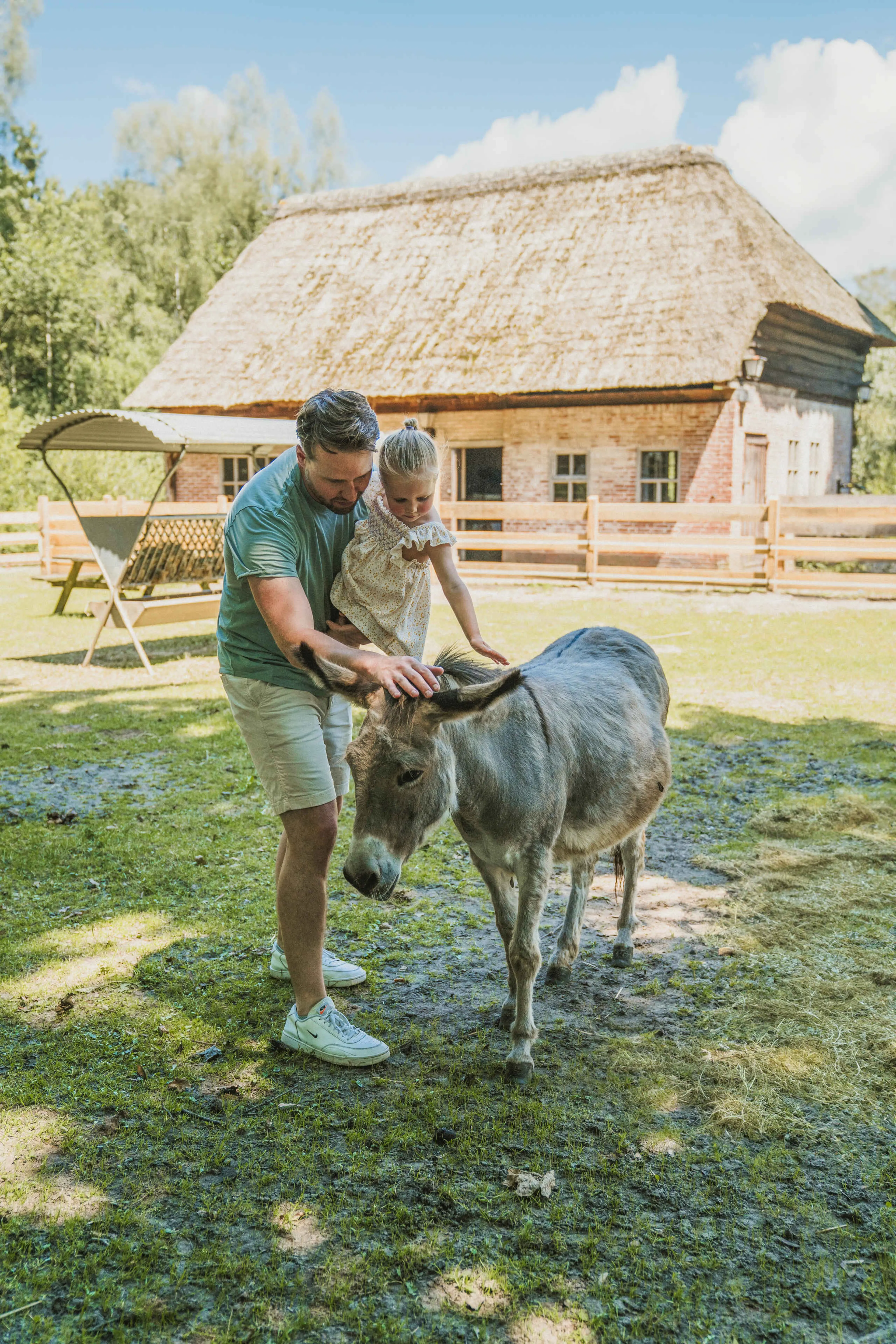 Een vader en zijn dochter aaien een ezel op de kinderboerderij bij Vakantiepark Dierenbos