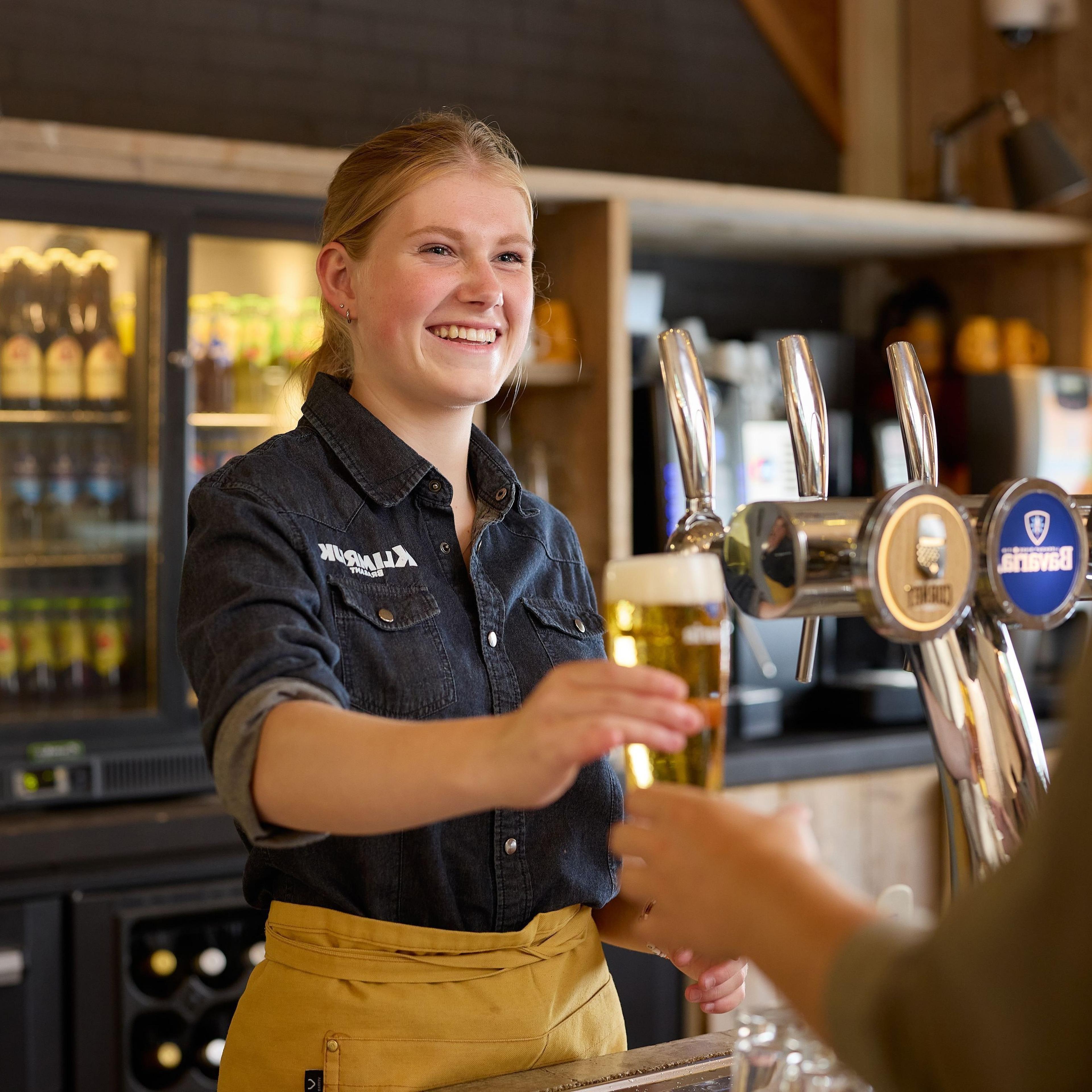Een barvrouw serveert een biertje bij Klimrijk Brabant.