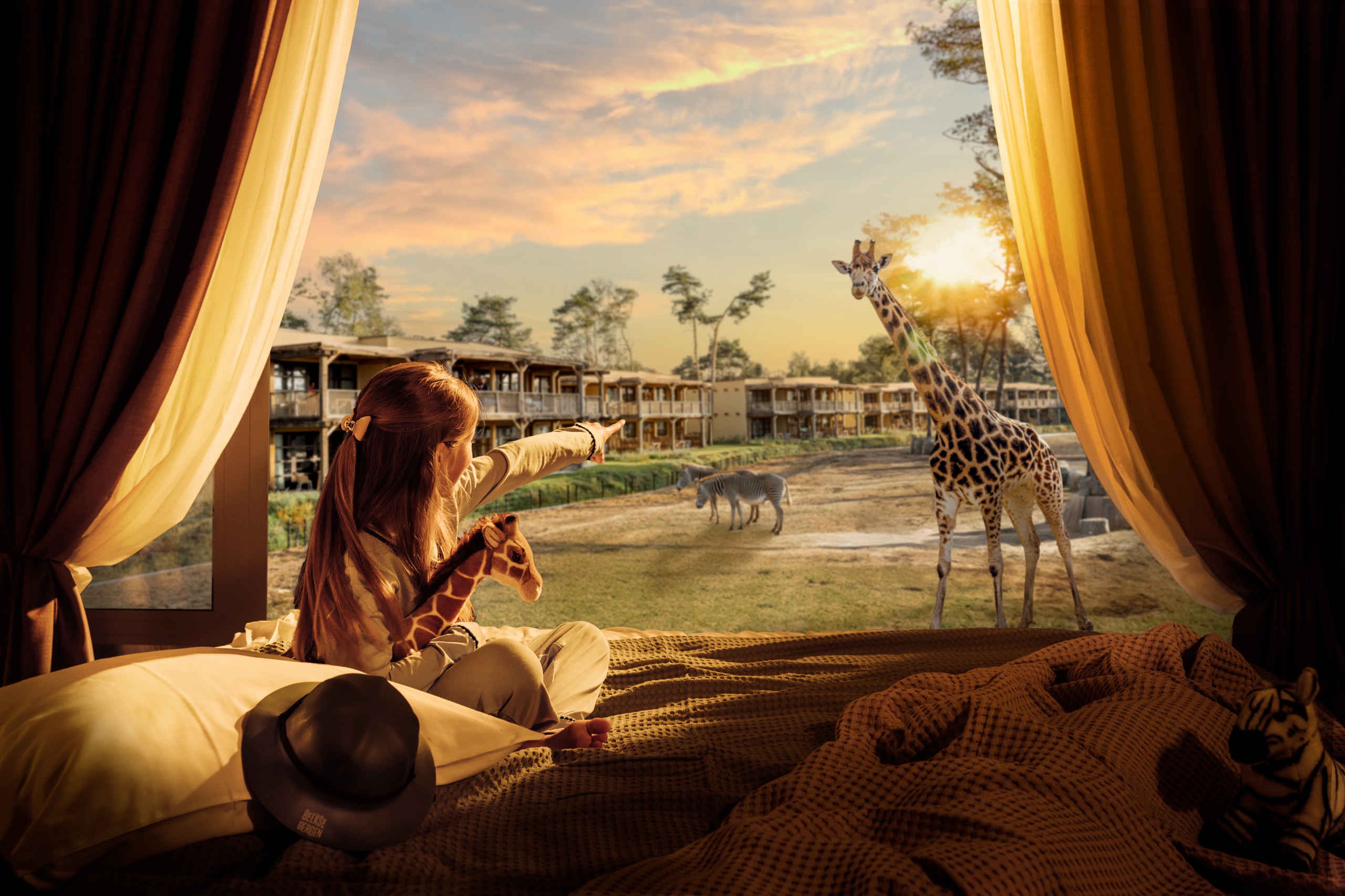 Een meisje kijk naar een giraffe op de savanne vanuit haar hotelkamer in Safari Hotel Beekse Bergen.