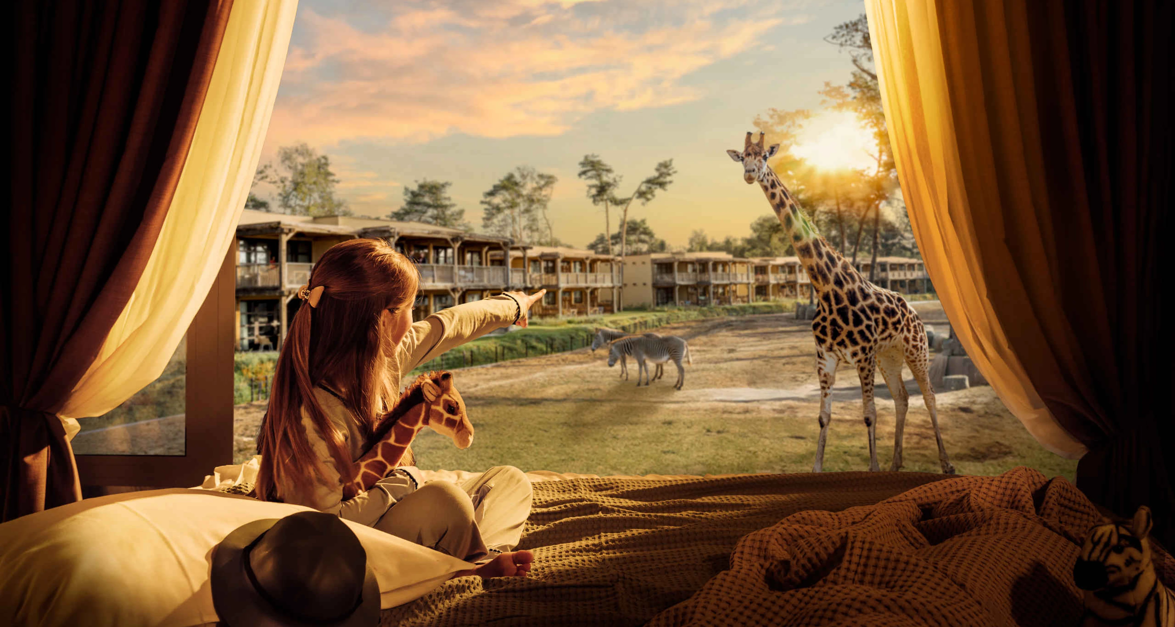 Een meisje kijk naar een giraffe op de savanne vanuit haar hotelkamer in Safari Hotel Beekse Bergen.