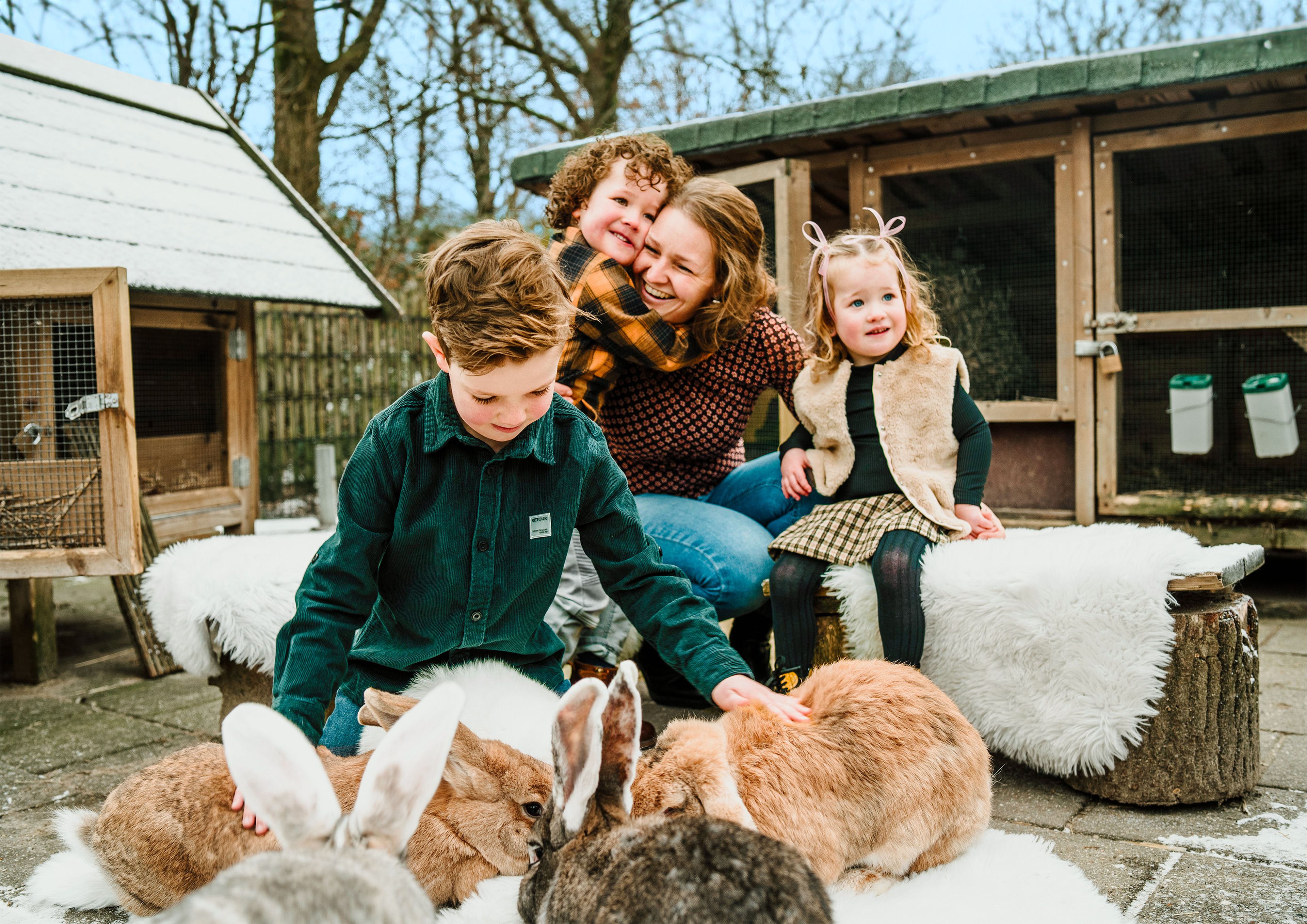 Een vrouw en haar kinderen kijken op de kinderboerderij bij de konijntjes op Vakantiepark Dierenbos