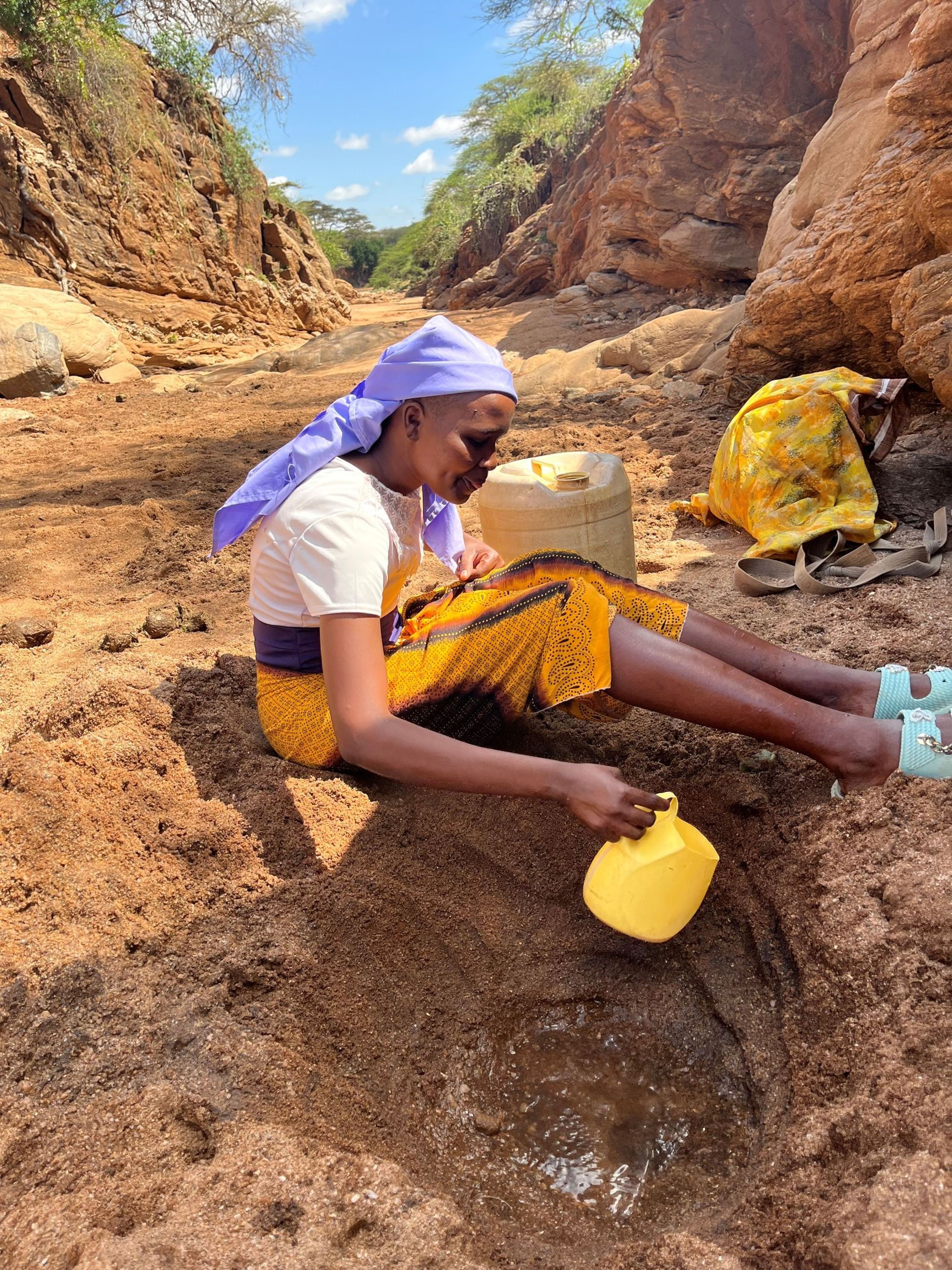 Een meisje vult een kan water in de rivierbedding in Kenia.