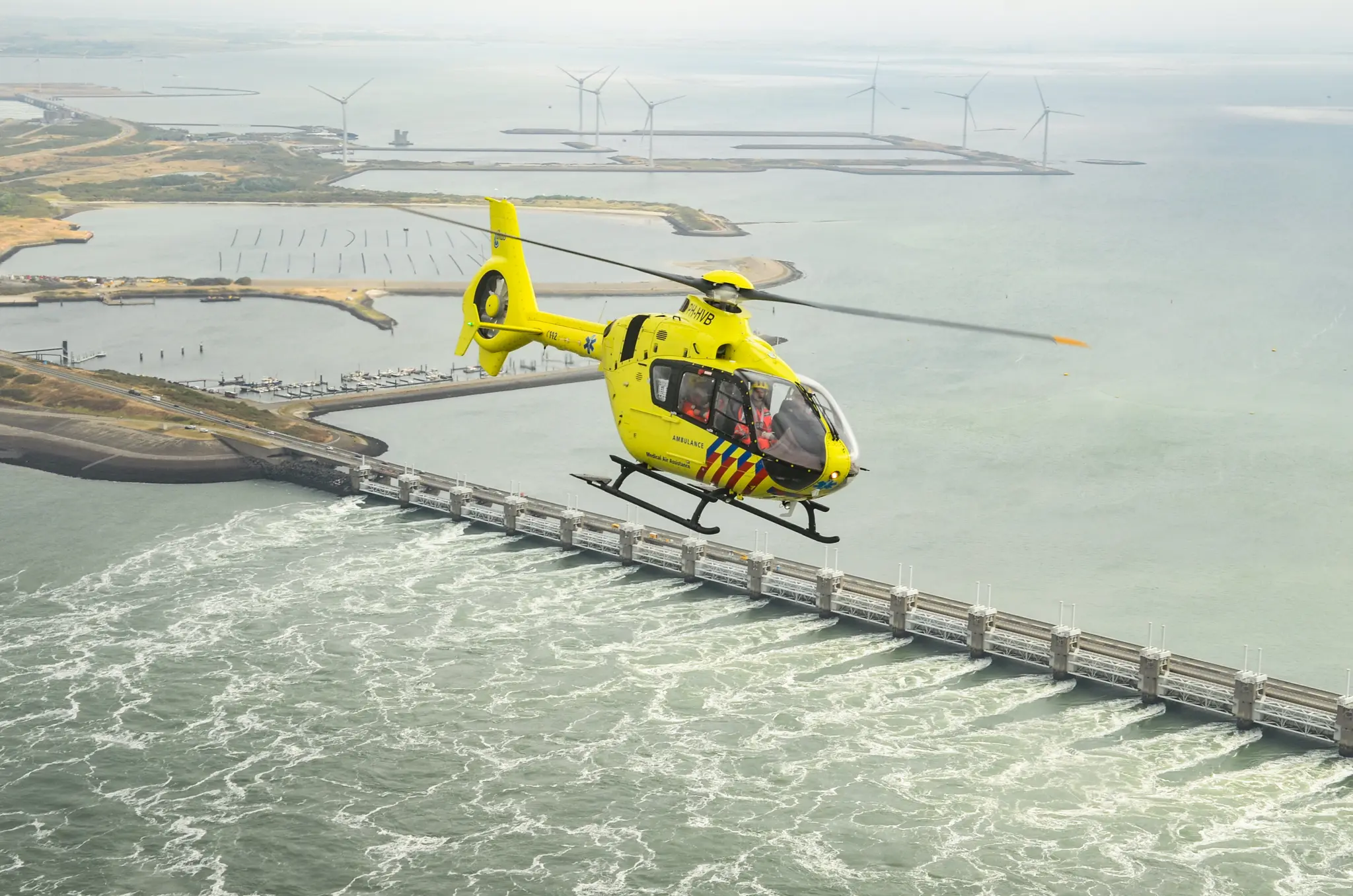 Een ANWB Medical Air Assistance traumahelikopter vliegend over de oosterscheldekering. Nu te zien tijdens de tentoonstelling in Aviodrome.