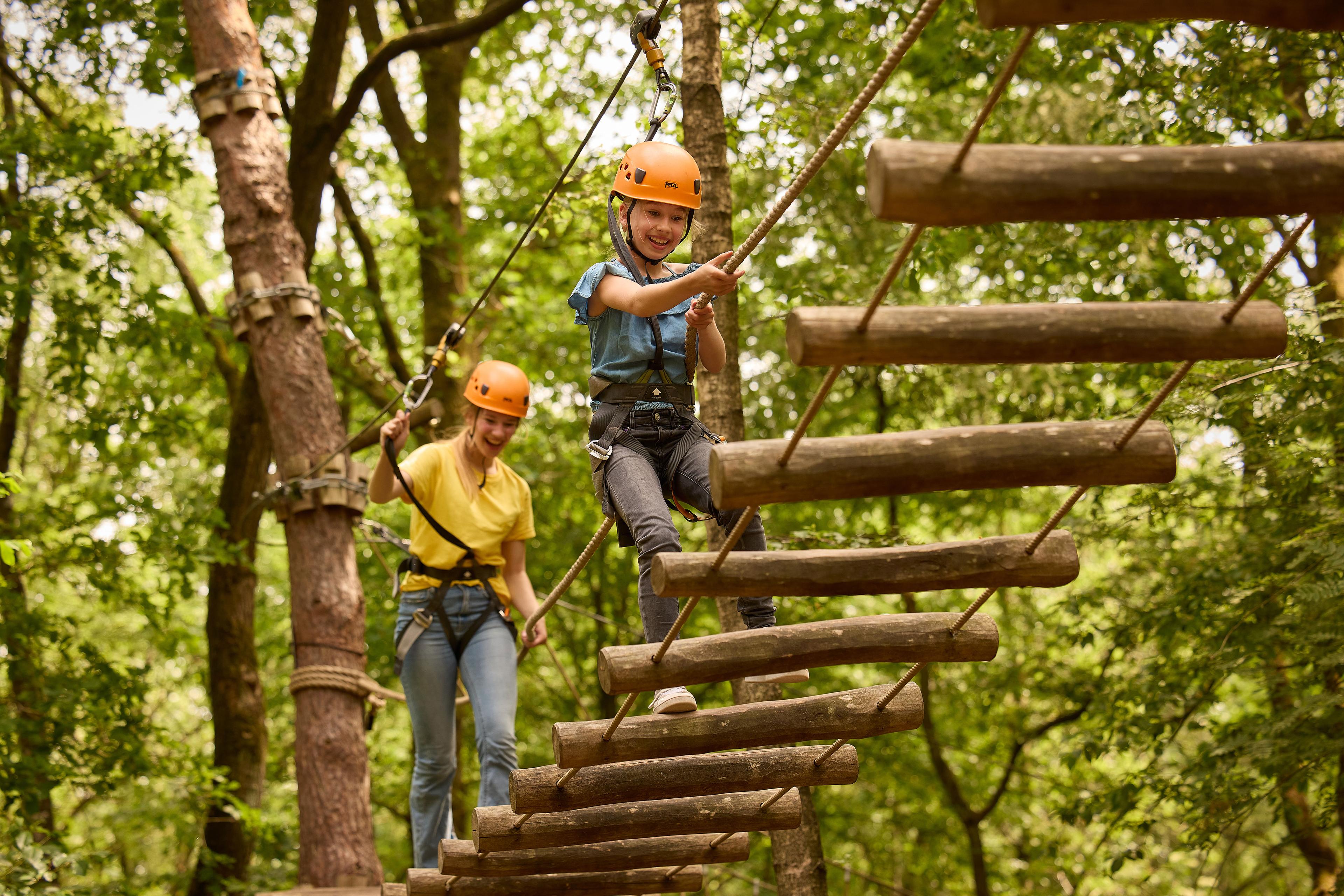 Kinderen op loopbrug met boomstammen op klimparcours bij Klimrijk Brabant