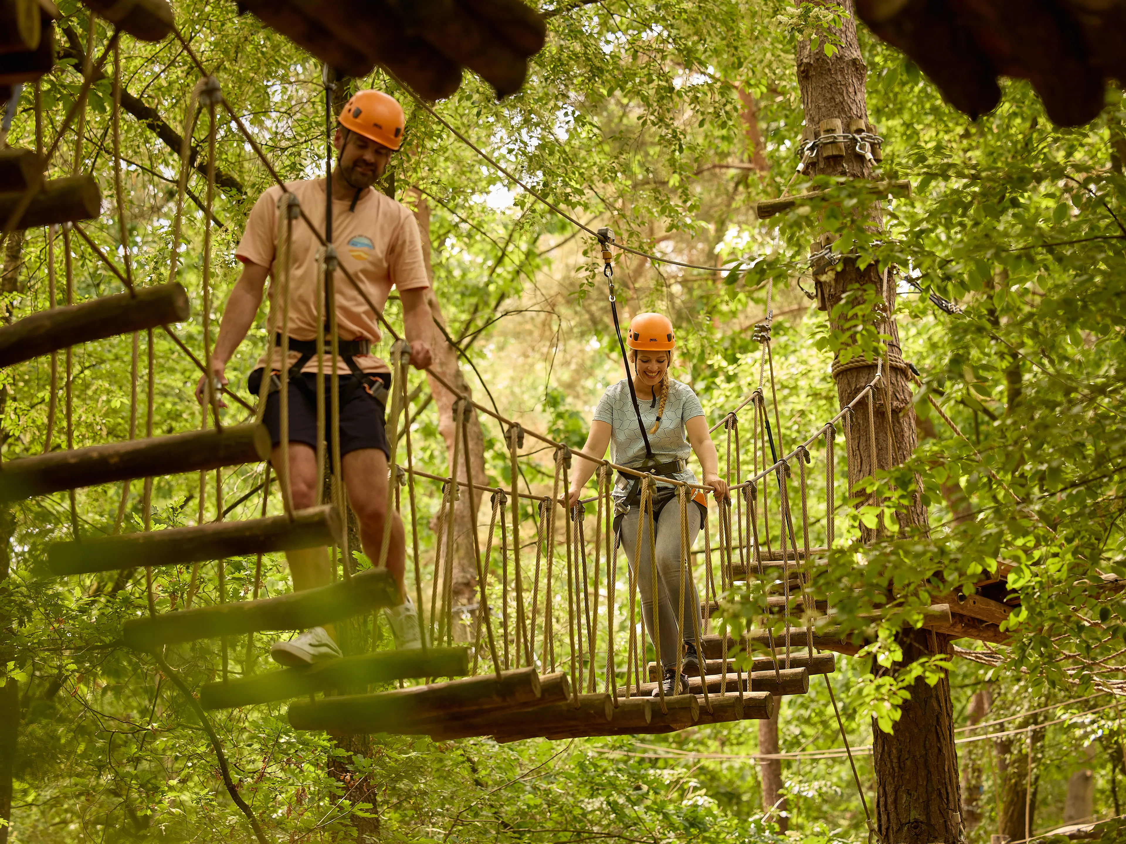 Man en vrouw op loopbrug met boomstammen op klimparcours bij Klimrijk Brabant