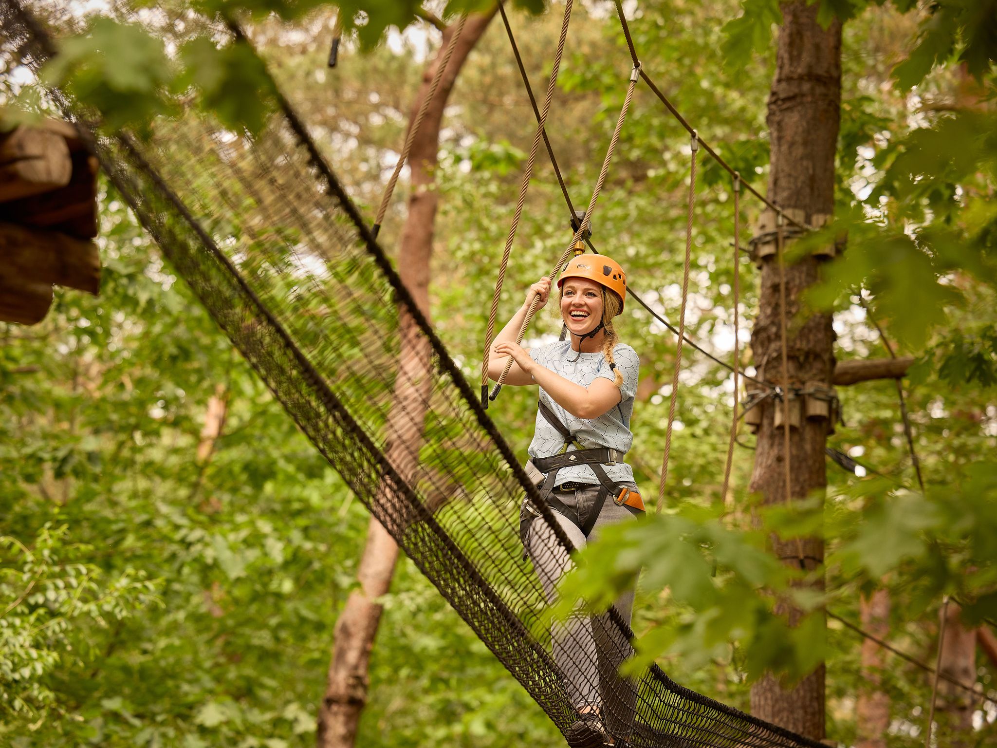 Vrouw met helm op een net op het klimparcours tussen de bomen bij Klimrijk Brabant
