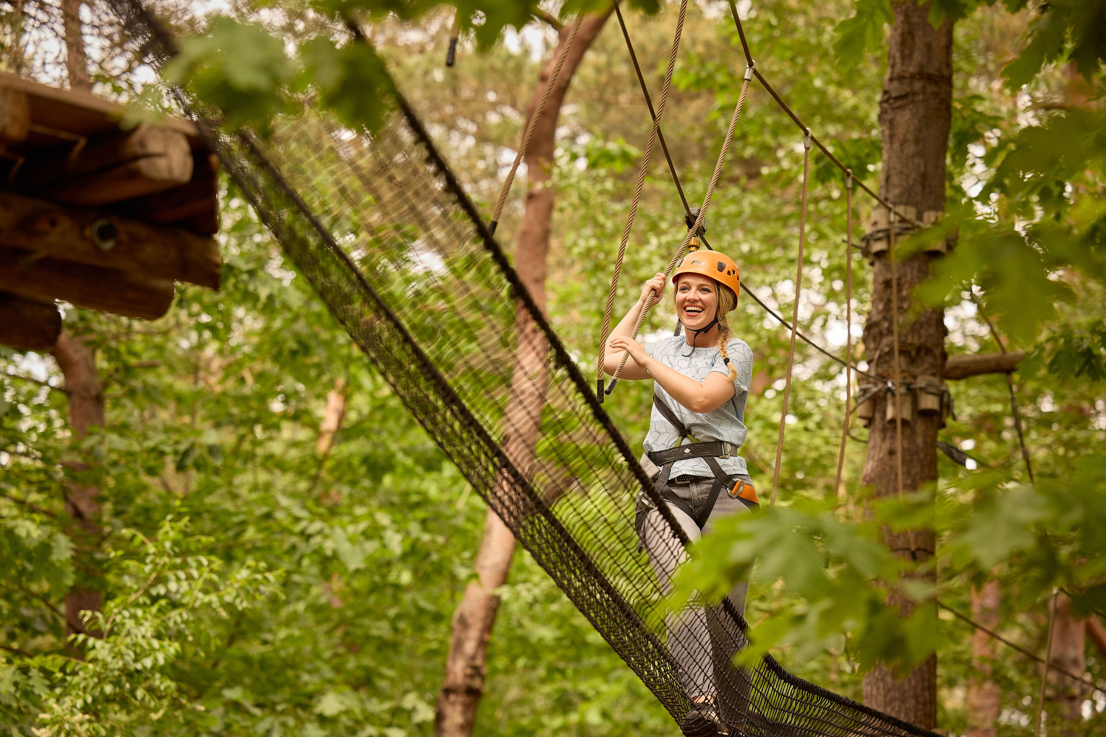 Vrouw met helm op een net op het klimparcours tussen de bomen bij Klimrijk Brabant