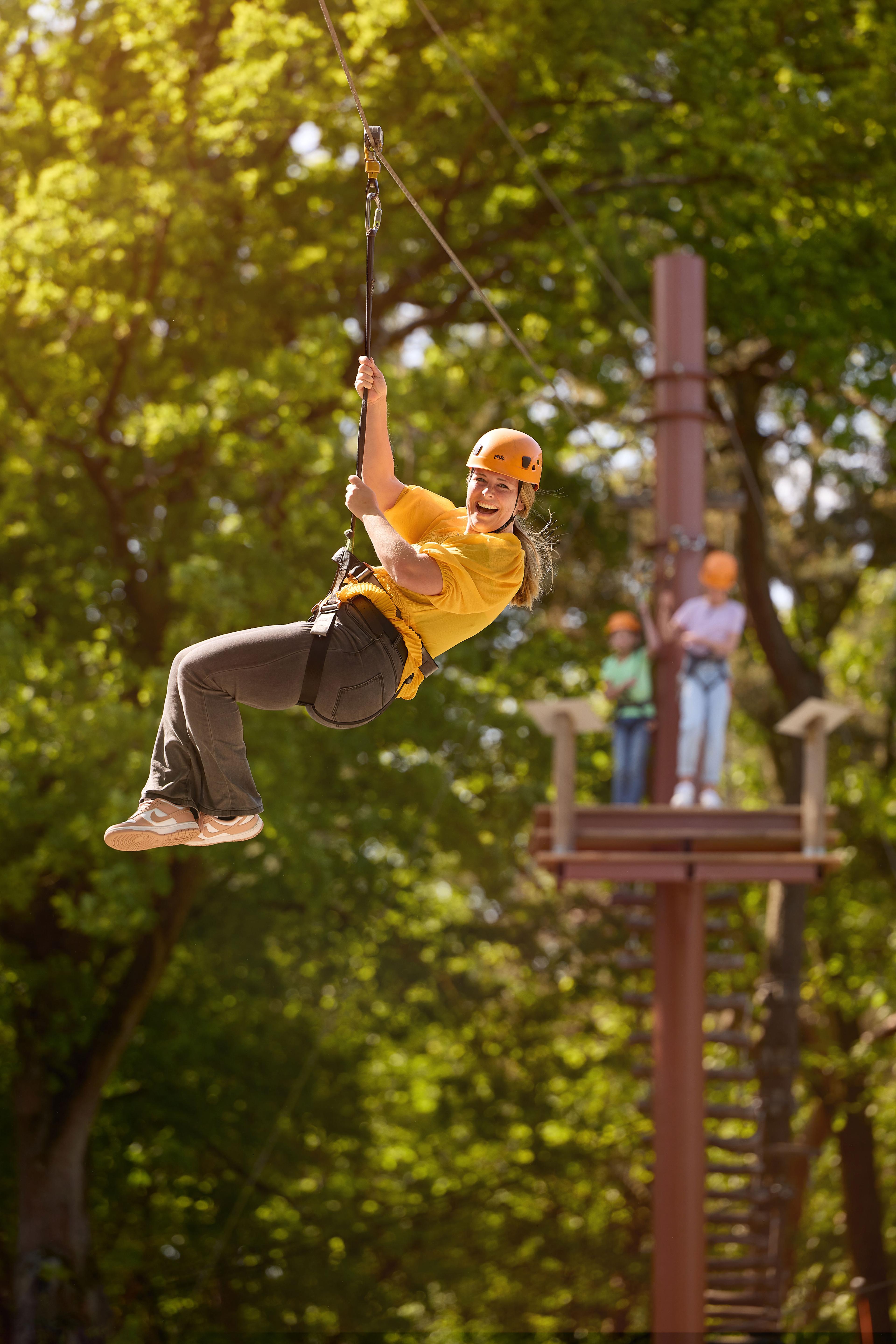 Vrouw op zipline tussen de bomen van het klimparcours bij Klimrijk Brabant