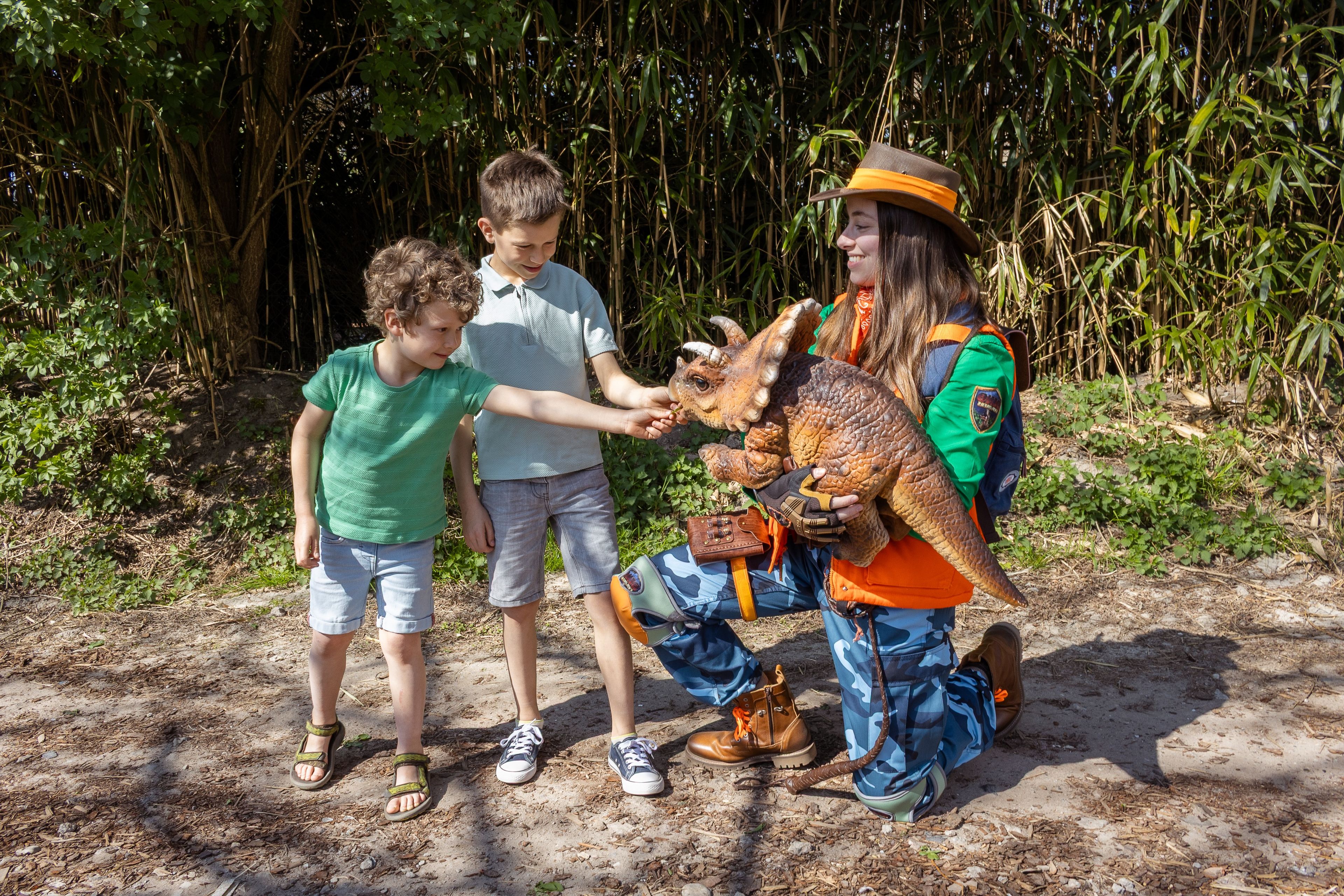 Een ranger met een baby triceratops staat bij twee kinderen die de dino aaien bij DINO vs DIER in Eindhoven Zoo.