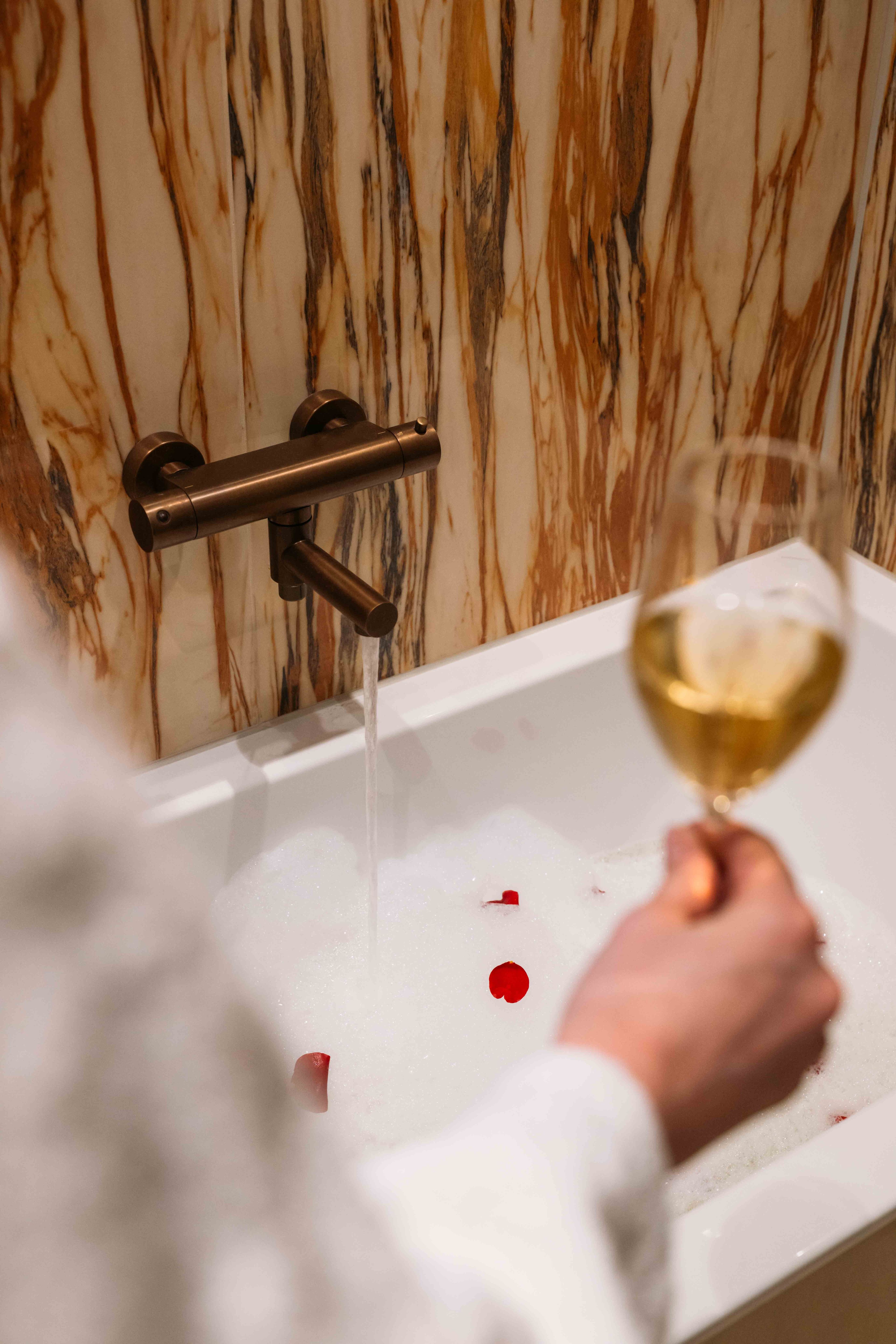 Champagne in de badkamer met een bad met rozenblaadjes in Kasteel Steenenburg