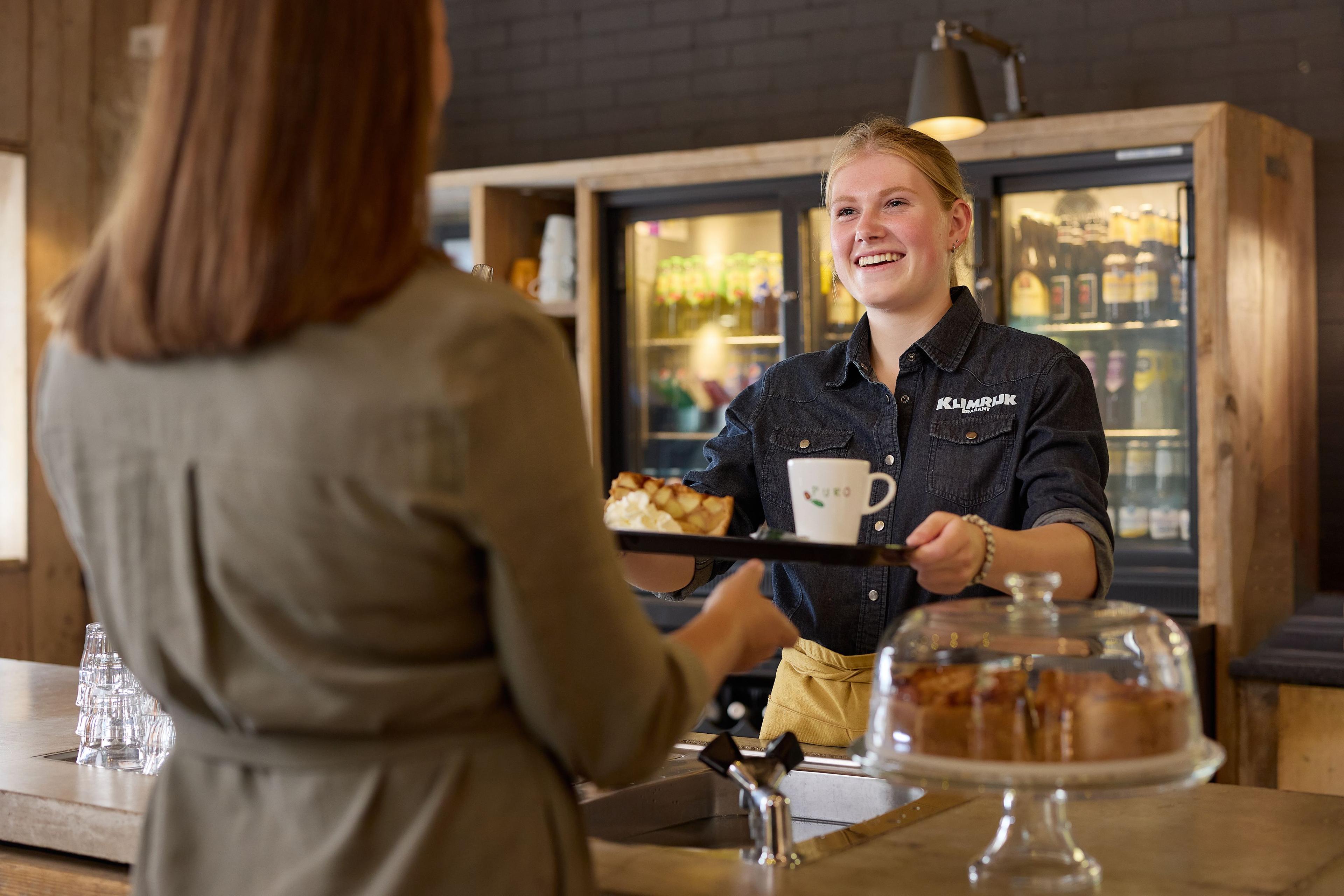 Medewerker overhandigd koffie aan bezoeker bij Klimrijk Brabant