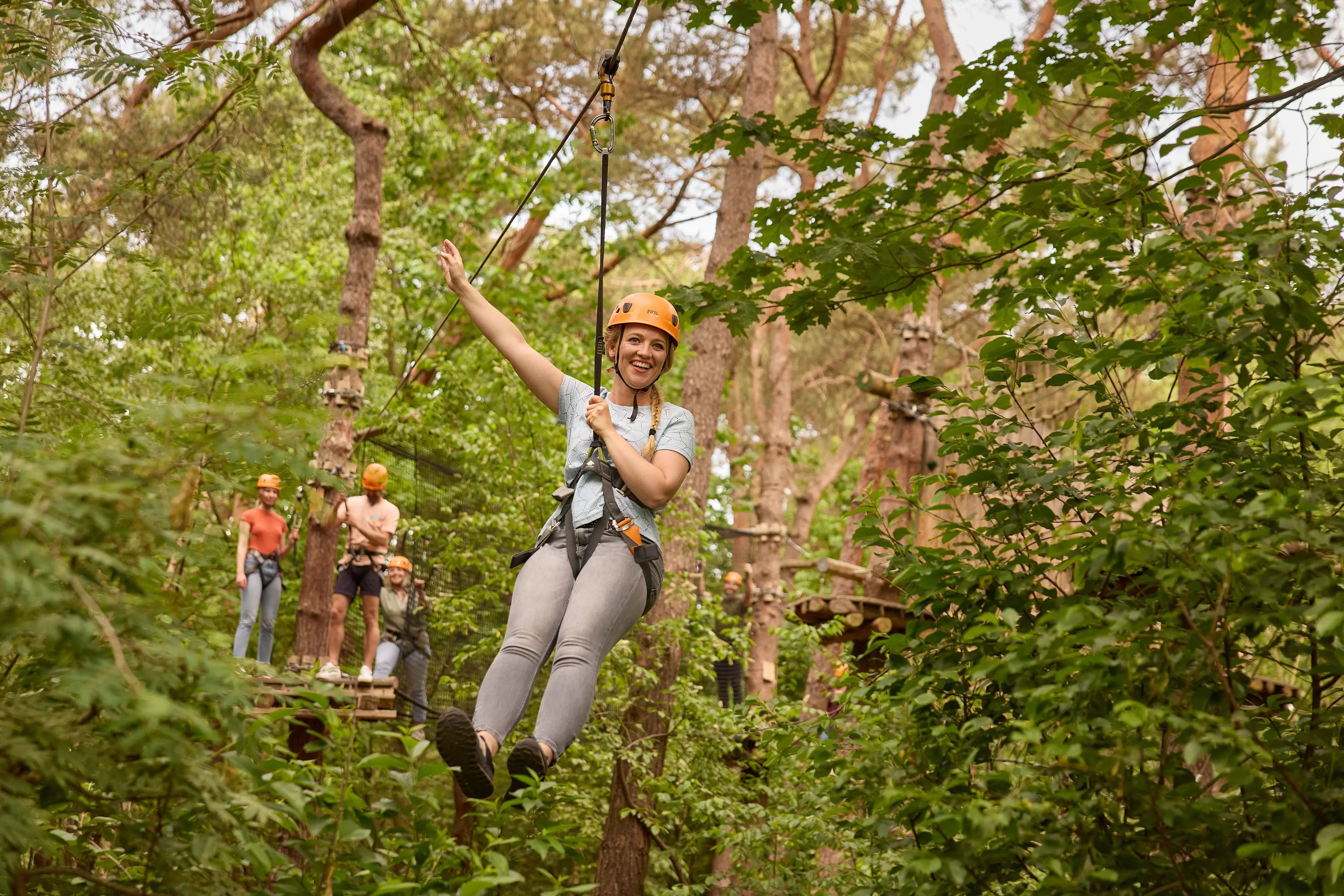Vrouw op zipline van klimparcours tussen struiken bij Klimrijk Brabant