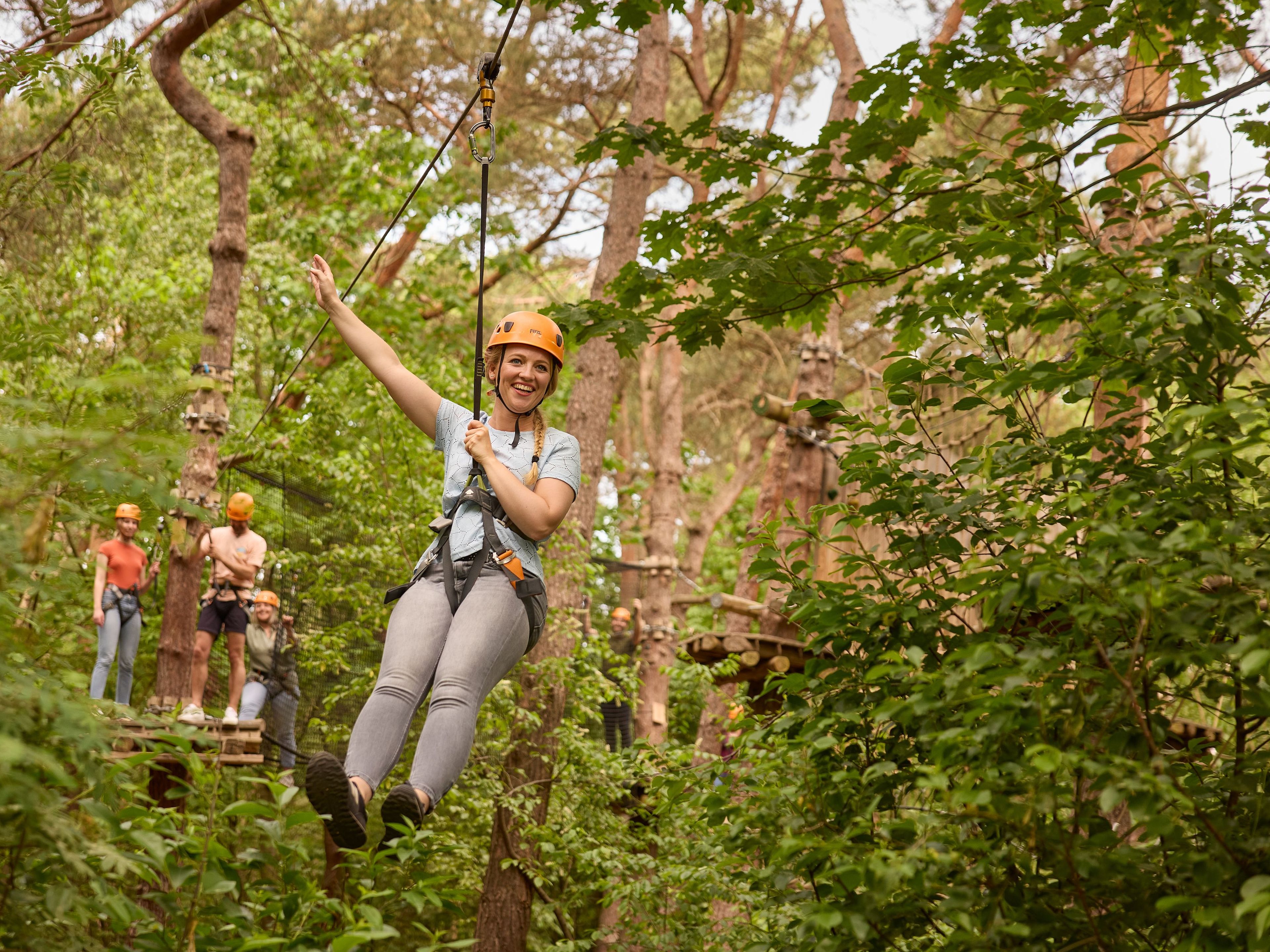 Vrouw op zipline van klimparcours tussen struiken bij Klimrijk Brabant