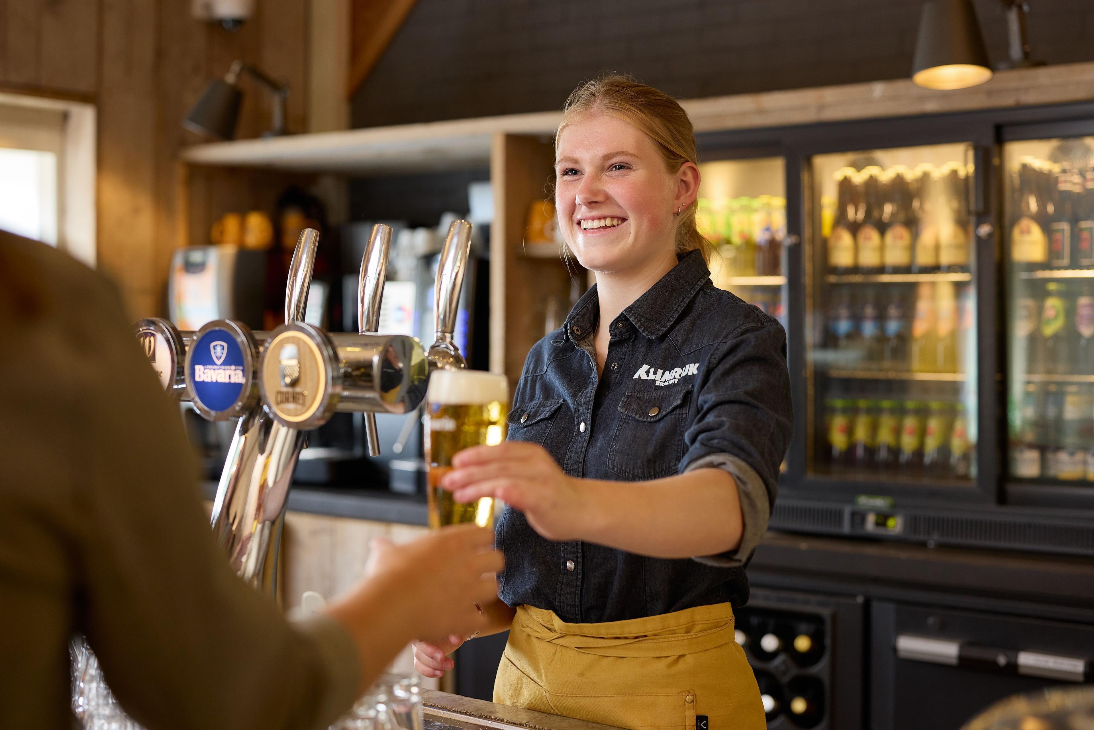 Medewerkster van het restaurant geeft een biertje aan gast bij Klimrijk Brabant
