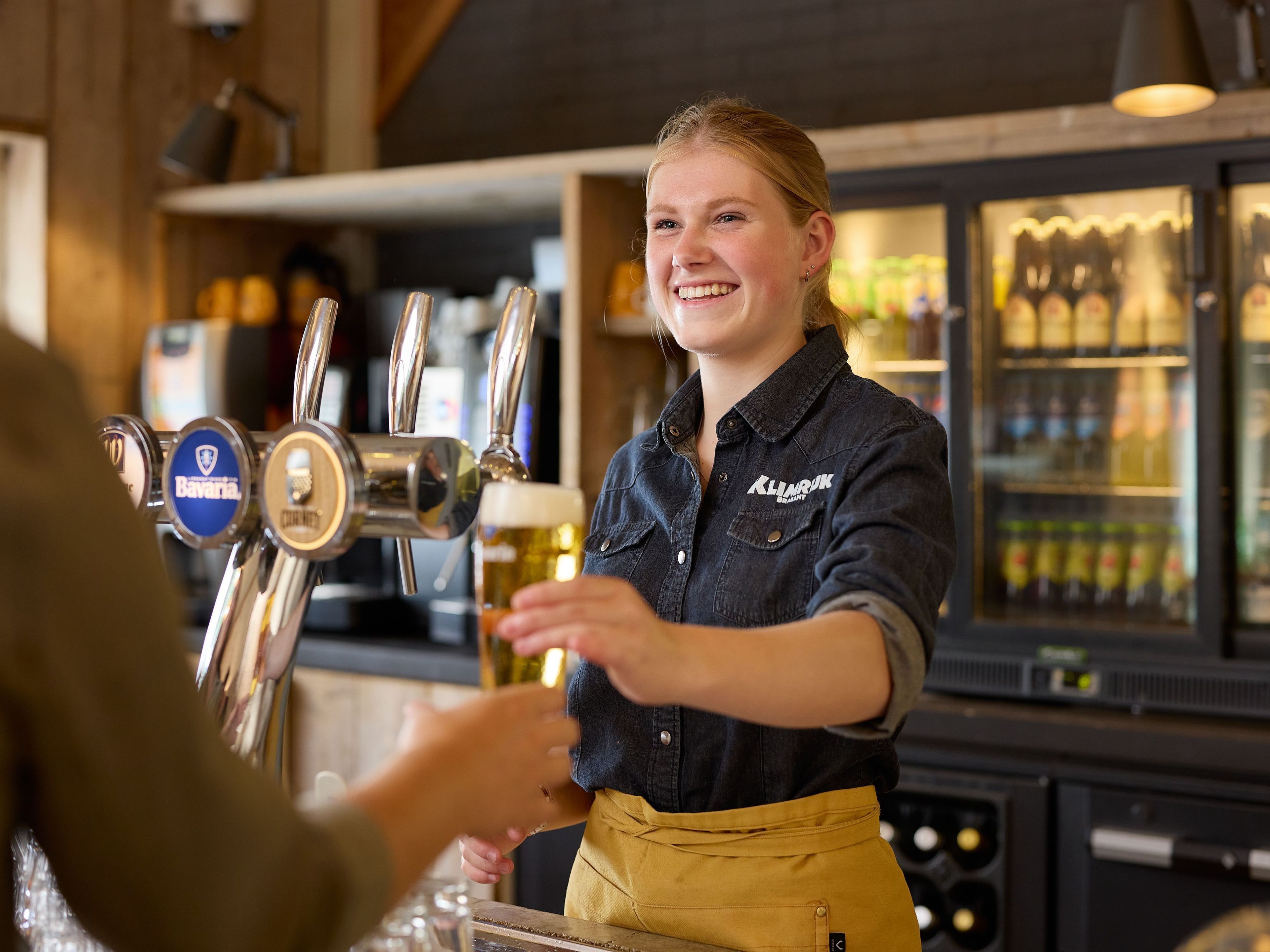 Medewerkster van het restaurant geeft een biertje aan gast bij Klimrijk Brabant
